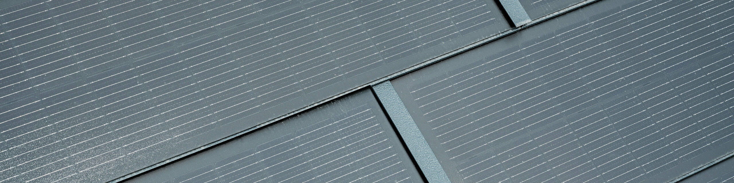 Detailaufnahme von PREFA Solardachplatten in Anthrazit. Die feinen Linien der Solarzellen sind deutlich sichtbar und fügen sich harmonisch in das Gesamtdesign ein. Diese ansprechende Integration von Solartechnologie in die Dachbedeckung vereint Funktionalität mit moderner Ästhetik und bietet eine umweltfreundliche Energiequelle für Gebäude.