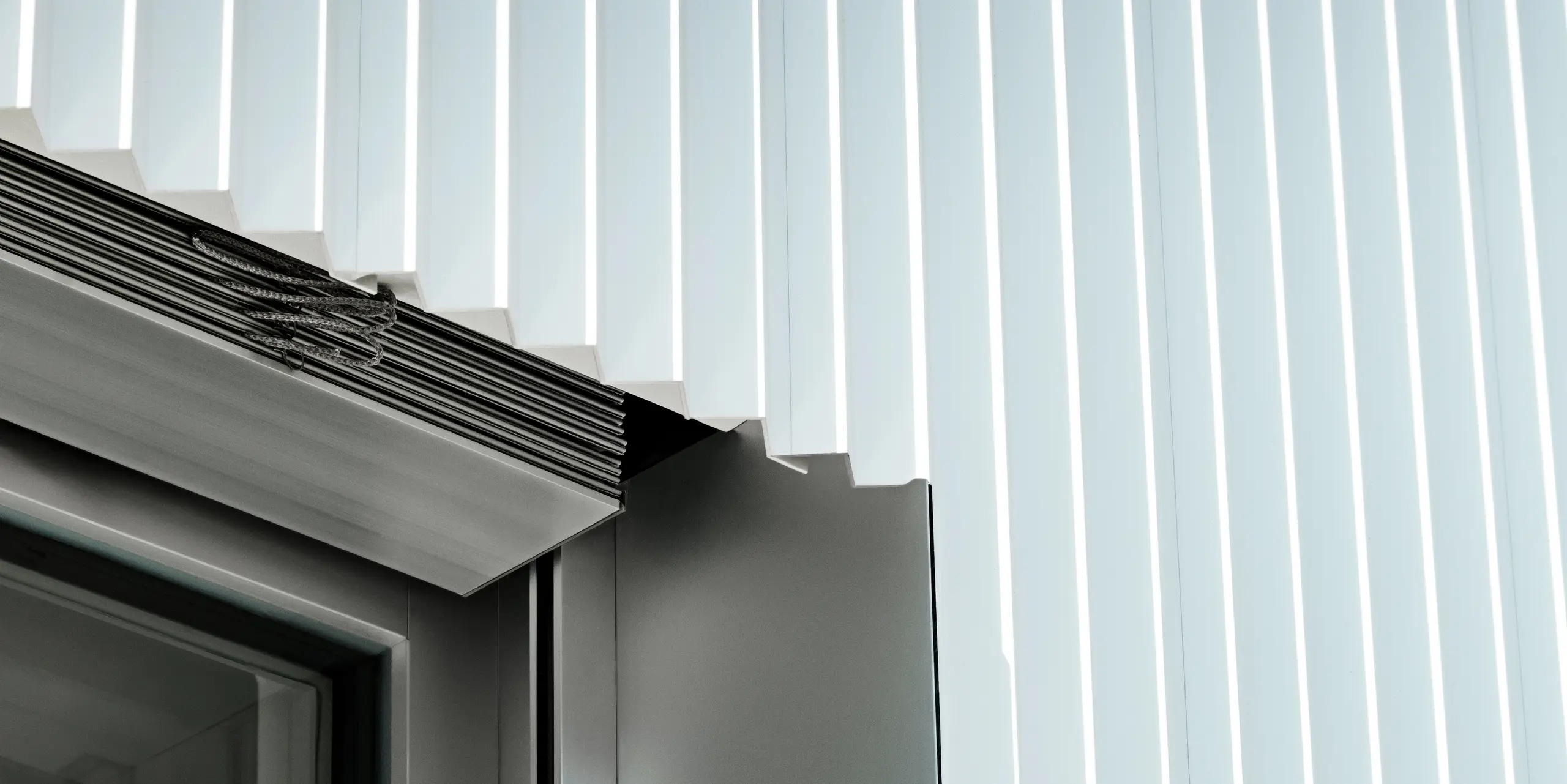 Präzise Detailaufnahme einer Fensterlaibung mit PREFA Zackenprofil in P.10 Reinweiß. Die klar geformten Aluminiumprofile treffen exakt auf das Fenster, das mit integrierter Raffstoreführung ergänzt ist. Die hochwertige Ausführung zeigt die perfekte Verarbeitung, Langlebigkeit und Witterungsbeständigkeit der PREFA Fassadensysteme – ideal für moderne Architektur mit Anspruch.