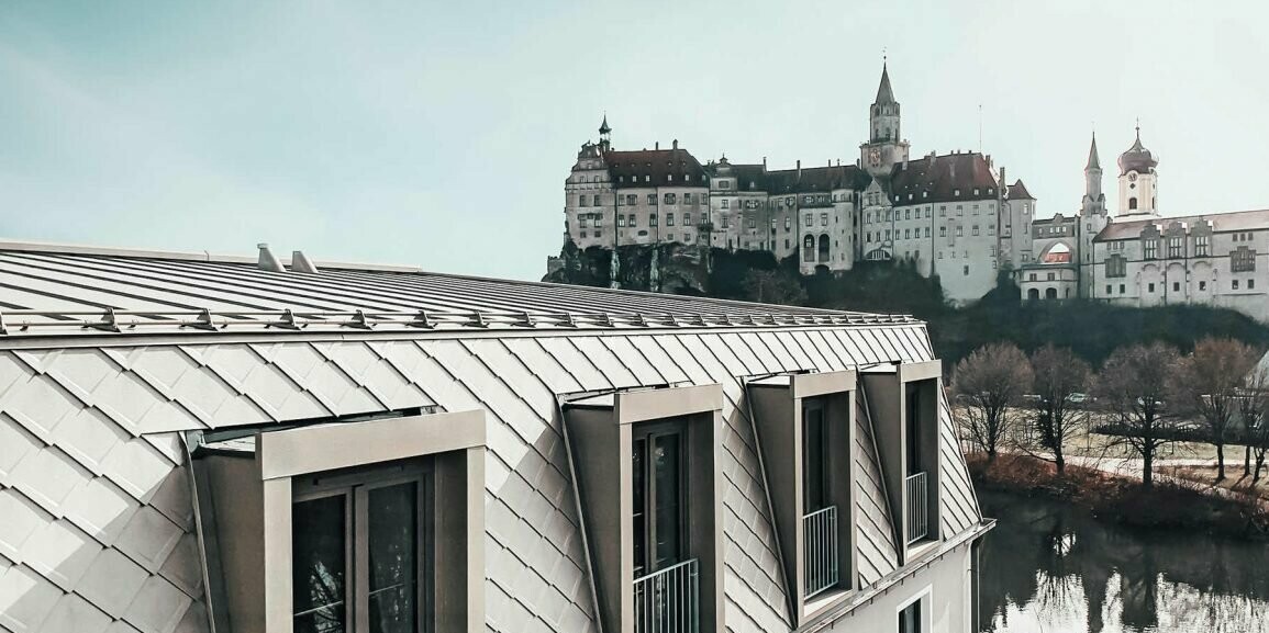 Im Vordergrund ist das PREFA Dach in der Farbe Bronze des Karls Hotel Sigmaringen zu sehen und im Hintergrund erstreckt sich die anliegende Schlossanlage Sigmaringen.