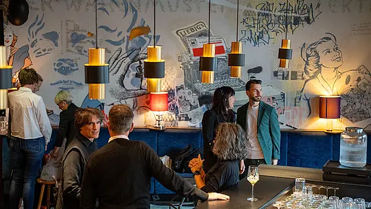 PREFARENZEN Special Wien: In gemütlicher Lounge-Atmosphäre tauschen sich Architekten und Planer bei Gesprächen und Networking aus. Warme Lichtakzente, modernes Interieur und kreative Wandgestaltung prägen die Szene. Das Event verbindet inspirierenden Austausch über Architektur, Design und nachhaltiges Bauen mit den innovativen PREFA Aluminiumlösungen für langlebige und zukunftsfähige Gebäude.