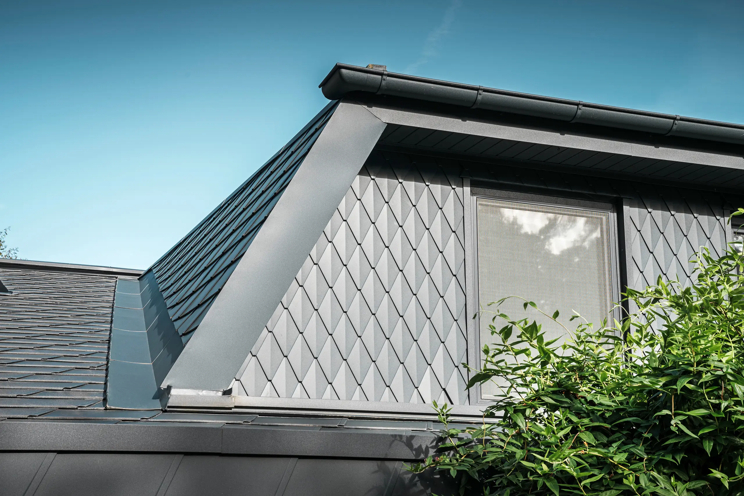 Trapezgaube eines Einfamilienhauses in Mechernich, verkleidet mit kleinen PREFA Dachrauten in P.10 Anthrazit. Das Dach ist mit PREFA Dachschindeln DS.19 in derselben Farbe gedeckt. Die hochwertige Aluminiumverkleidung sorgt für Wetterbeständigkeit und eine moderne, ästhetische Optik.