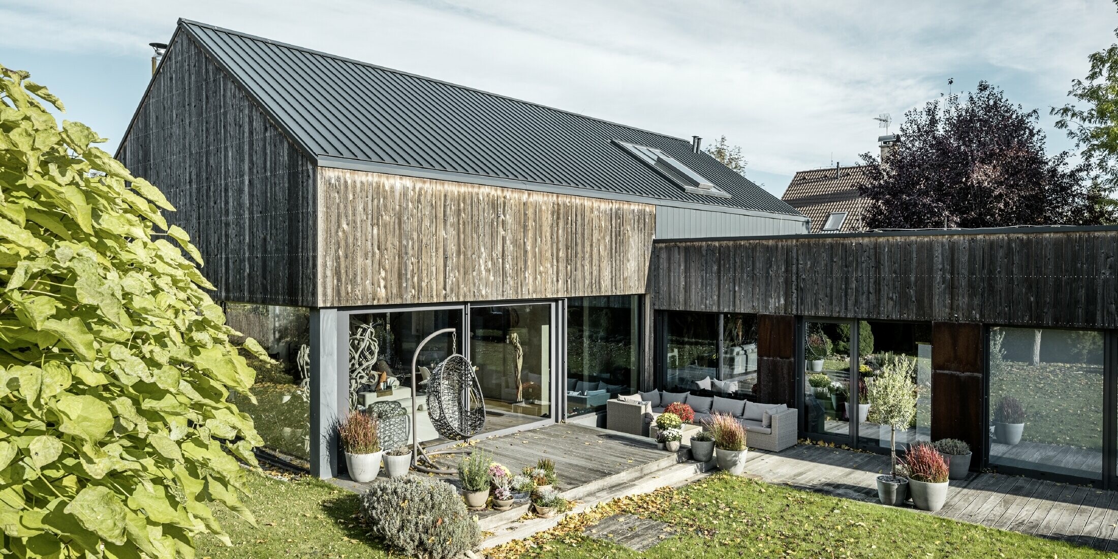 Einfamilienhaus mit Satteldach, eingedeckt mit Doppelstehfalz PREFALZ in Anthrazit und verwitterter Holzfassade. Mit schöner Holzterrasse und großen Fensterflächen im Erdgeschoss.