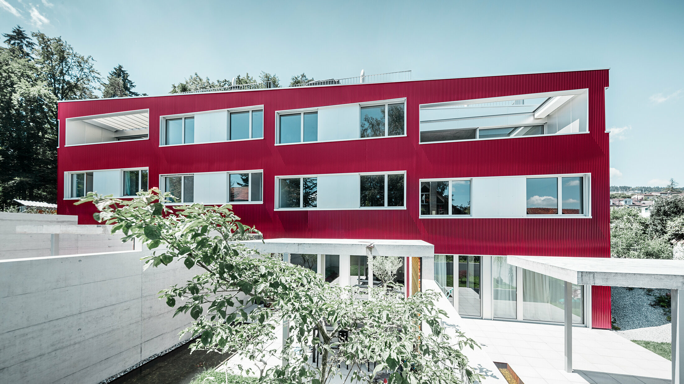Wohnhausanlage mit Flachdach und Balkonen mit weinroter Fassade mit PREFA Profilwelle 