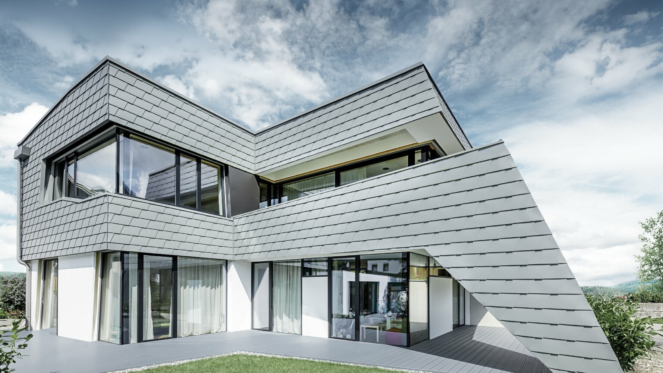 Modernes Einfamilienhaus mit Flachdach, großen Fensterflächen und einer Schindel-Fassade in hellgrau aus Aluminium von PREFA