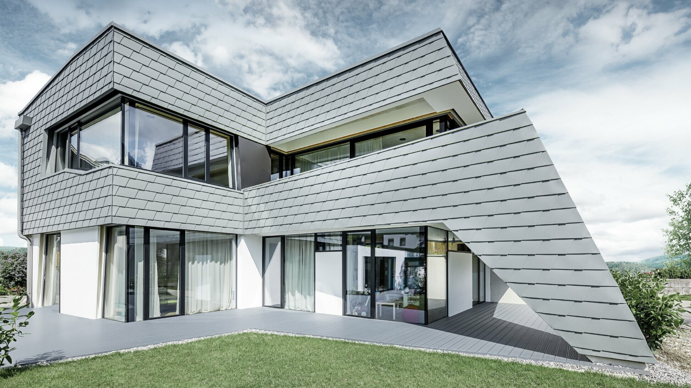 Modernes Einfamilienhaus mit Flachdach, großen Fensterflächen und einer Schindel-Fassade in hellgrau aus Aluminium von PREFA