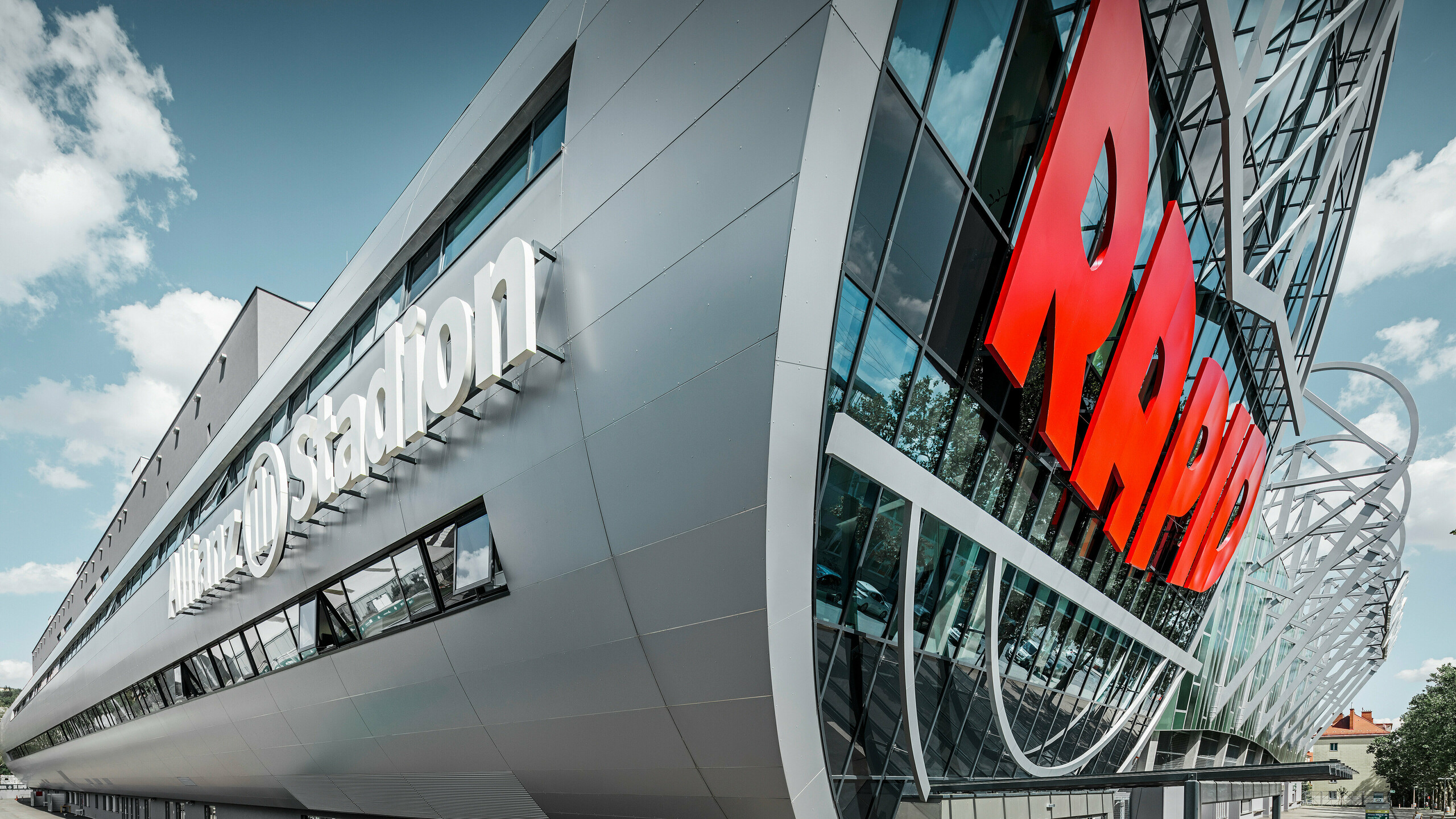 Nahaufnahme der Fassade des Allianz Stadions, Heimat des SK Rapid Wien. Die eindrucksvolle Röhre im Eingangsbereich präsentiert die PREFA Aluminium Verbundplatten in Silbermetallic. Der Blickwinkel unterstreicht die moderne Architektur. Durch den strahlend roten RAPID-Schriftzug und die klare Linienführung der silbernen Platten erhält die Röhre eine visuell beeindruckende Dynamik und Ästhetik. Auf diese Weise wird bereits beim Gang zum Stadion bei allen Fußball-Fans Leidenschaft entfacht.