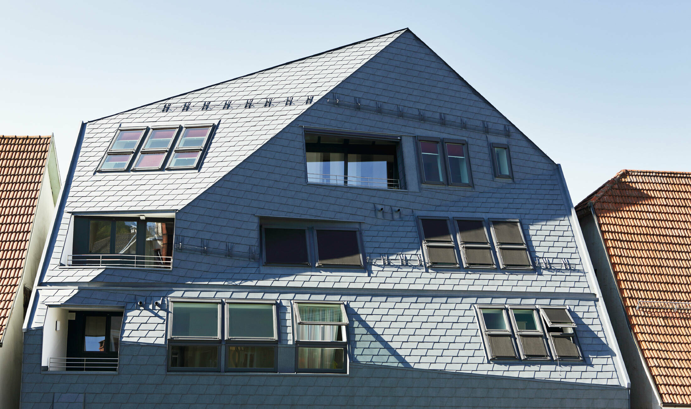 Galeriehaus mit gekanteter Fassadenfläche, verkleidet mit der PREFA Dach- und Wandschindel in P.10 Steingrau mit vielen Fenstern