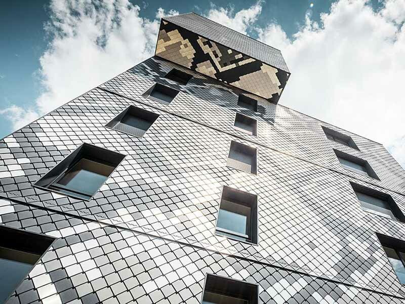 Anschicht vom Fuße des Gebäudes le Python in Grenoble, bekleidet mit der PREFA Aluminium Wandraute 20 × 20 in den Farben anthrazit, hellgrau, naturblank und silbermetallic, der Himmel ist leicht bewölkt
