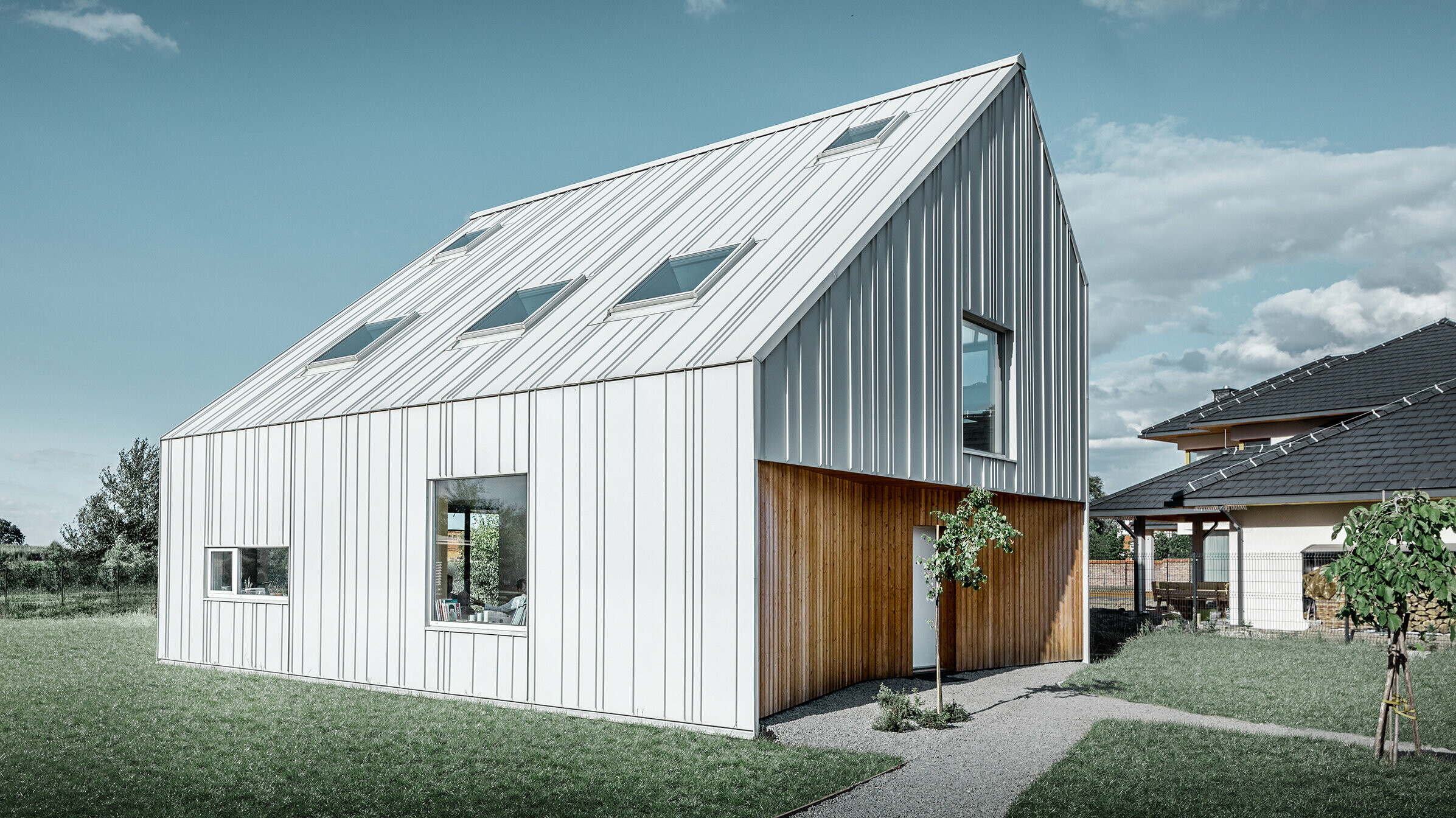 Modern geschnittenes Einfamilienhaus mit Satteldach, die komplette Außenhaut ist mit PREFALZ in Prefaweiß verkleidet. Dabei ziehen sich die unterschiedlich breiten Scharen vom Dach weiter über die Fassade. Im Dach sind mehrere Dachfenster verbaut.