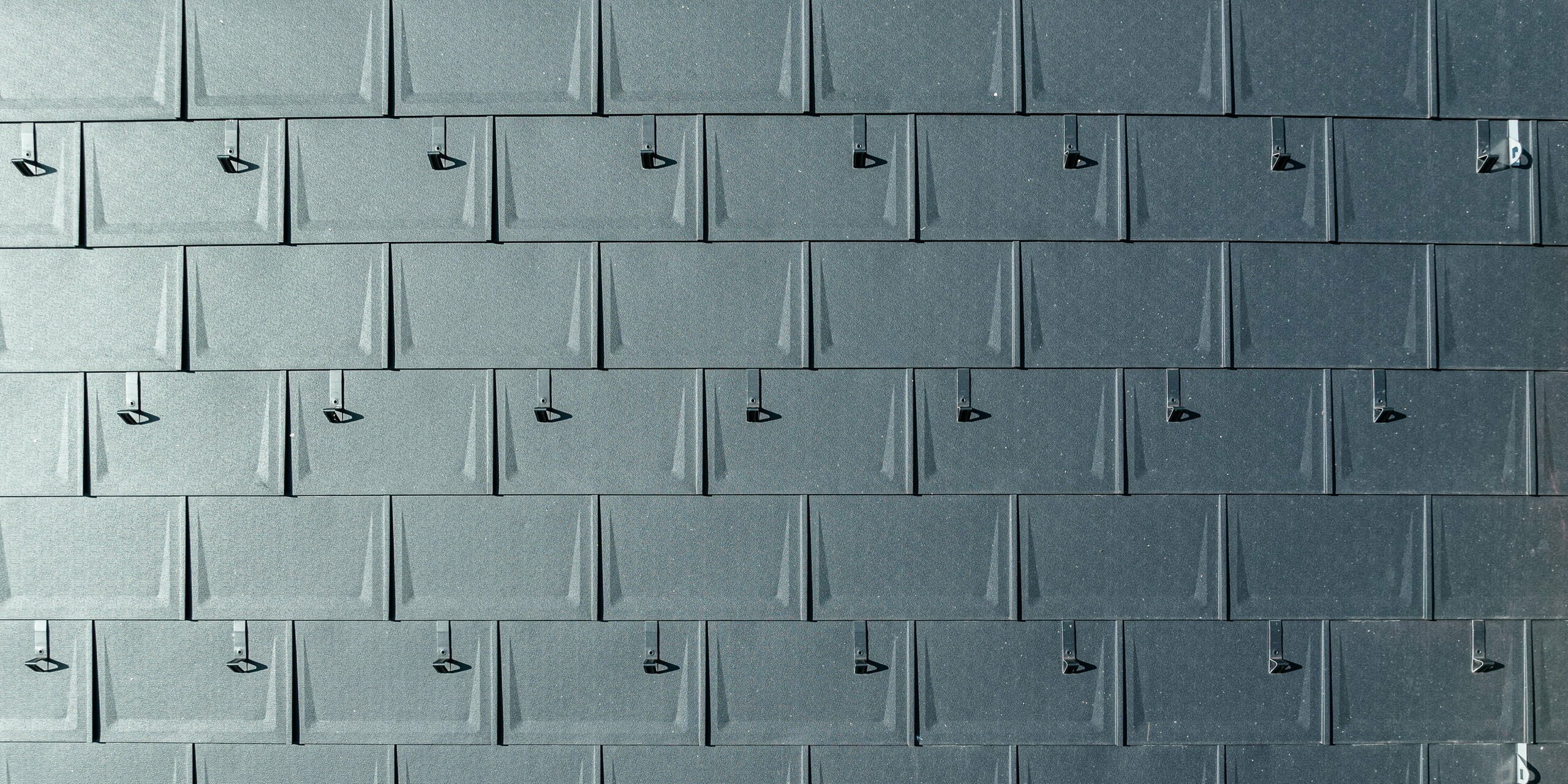 Nahaufnahme einer PREFA Dacheindeckung aus Aluminium. PREFA Dachplatten R.16 in der begehrten Farbe P.10 Anthrazit sind präzise miteinander verbunden. Die hochwertigen Aluminiumplatten bieten eine langlebige, witterungsbeständige und optisch ansprechende Dachlösung. Schneestopper sorgen für zusätzliche Sicherheit.