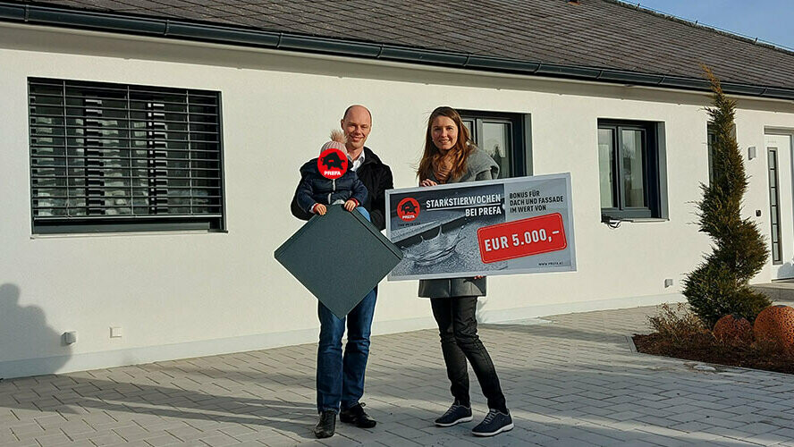 Familie mit Kind hält den Gewinnscheck in der Höhe von 5.000 Euro für PREFA Dach oder Fassade in der Hand