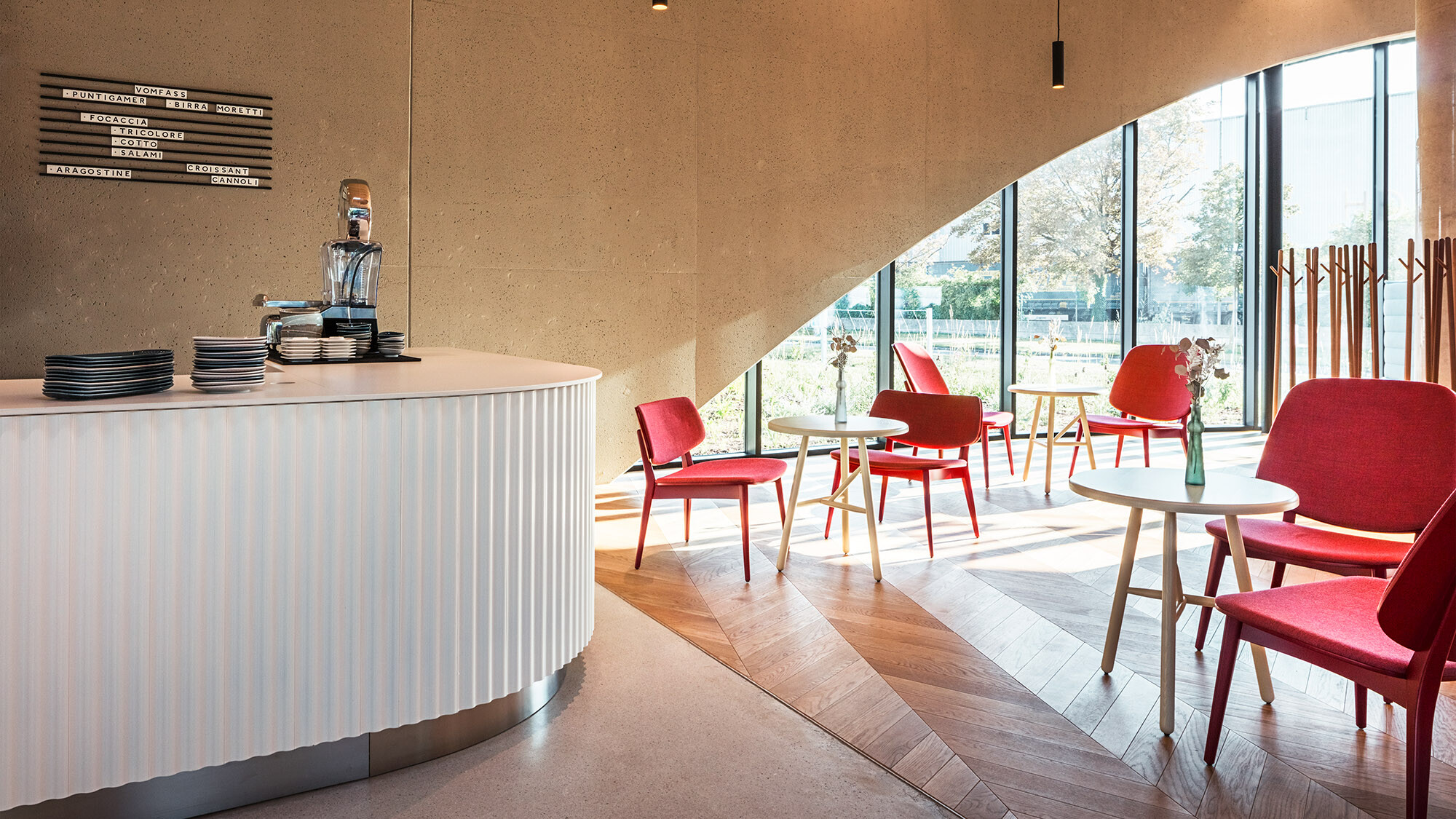 Einer der Räume des Restaurants mit einer Theke, roten Stühlen und einem Parkettboden, dahinter ist eines der Rundbogenfenster zu sehen.