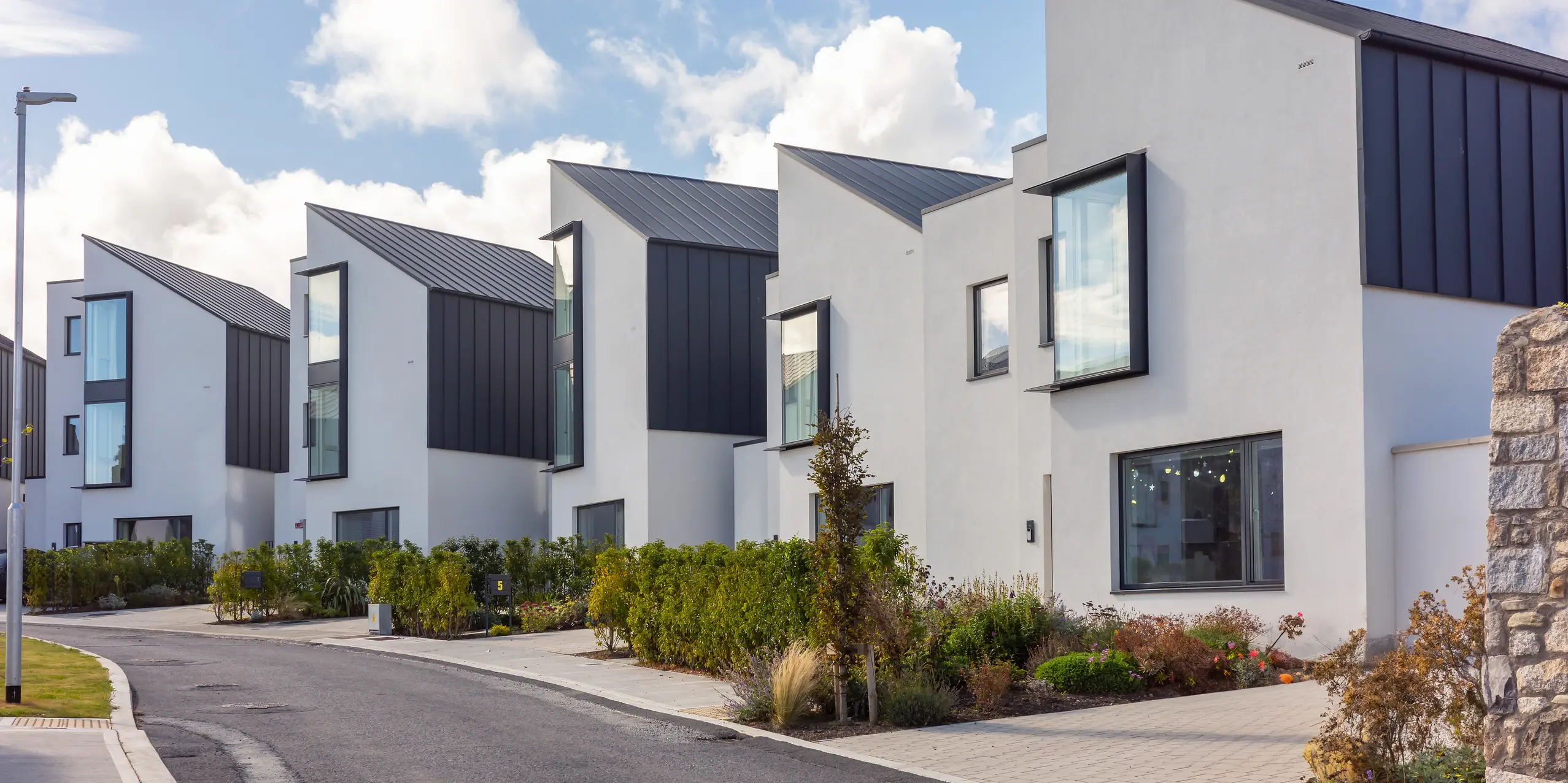 Reihenhäuser in Watson Place mit klarer, moderner Architektur und markanten PREFALZ Pultdächern und Fassaden in P.10 Anthrazit. Die scharf geschnittenen Dachlinien und großen Fensterelemente setzen dynamische Akzente. Die langlebigen PREFA Aluminiumoberflächen bieten optimalen Witterungsschutz und verleihen der Wohnanlage eine elegante, zeitlose Erscheinung.
