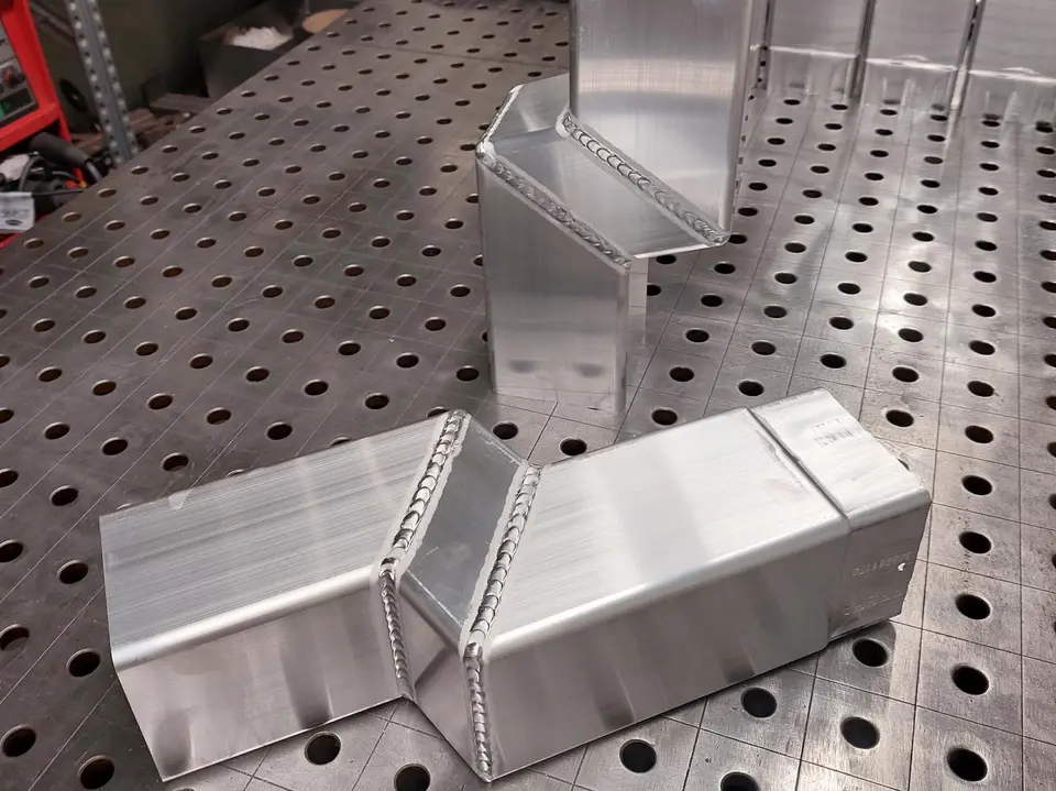 Zu sehen ist ein fertig geschweißtes Quadratrohr (Sockelknie) in Aluminium blank