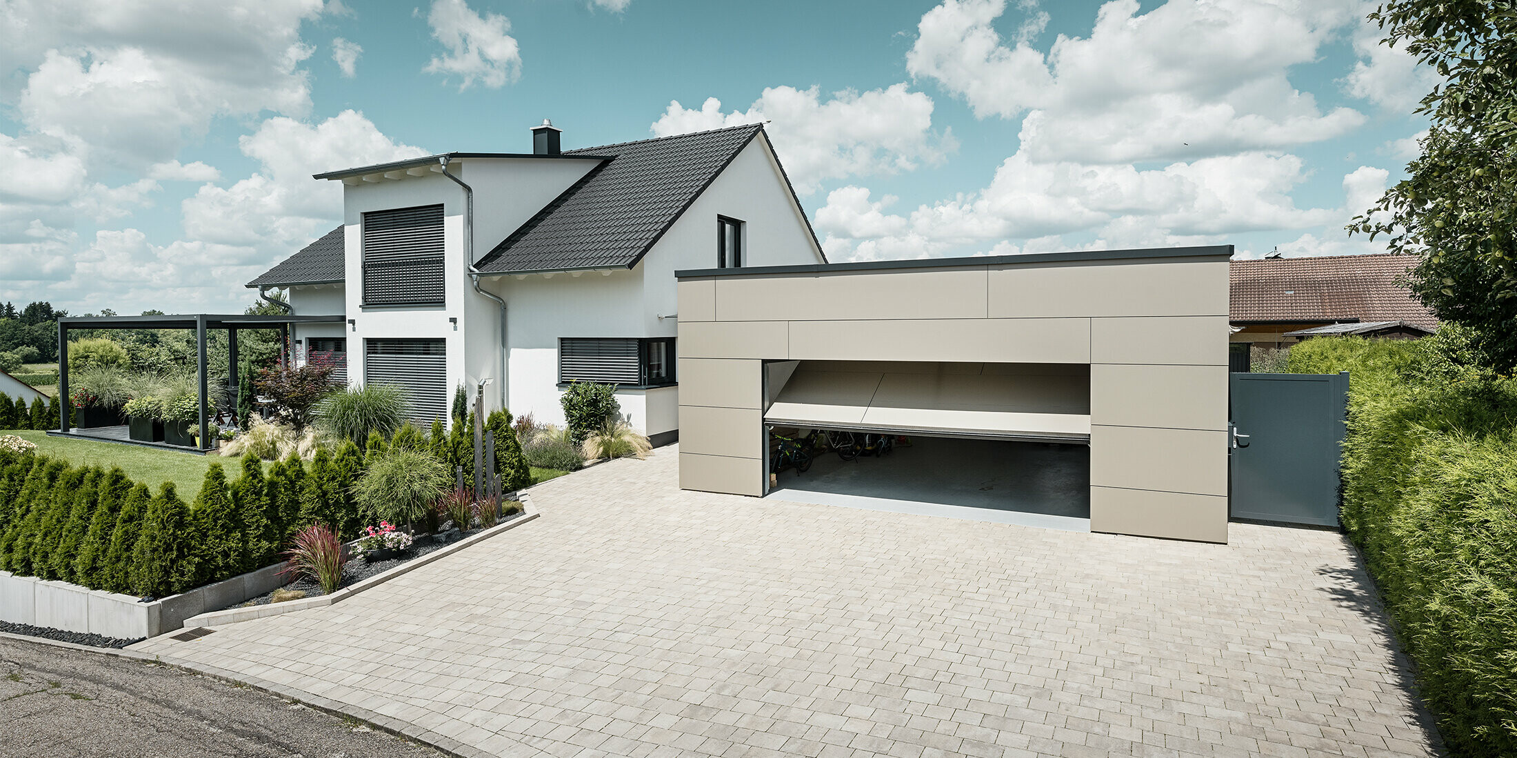 Die Fassade der Garage des Einfamilienhauses wurde komplett mit der PREFABOND Aluminium Verbundplatte in Bronze verkleidet. Das Garagentor ist geöffnet, davor ist eine große Einfahrt für mindestens 2 Autos gepflastert. 