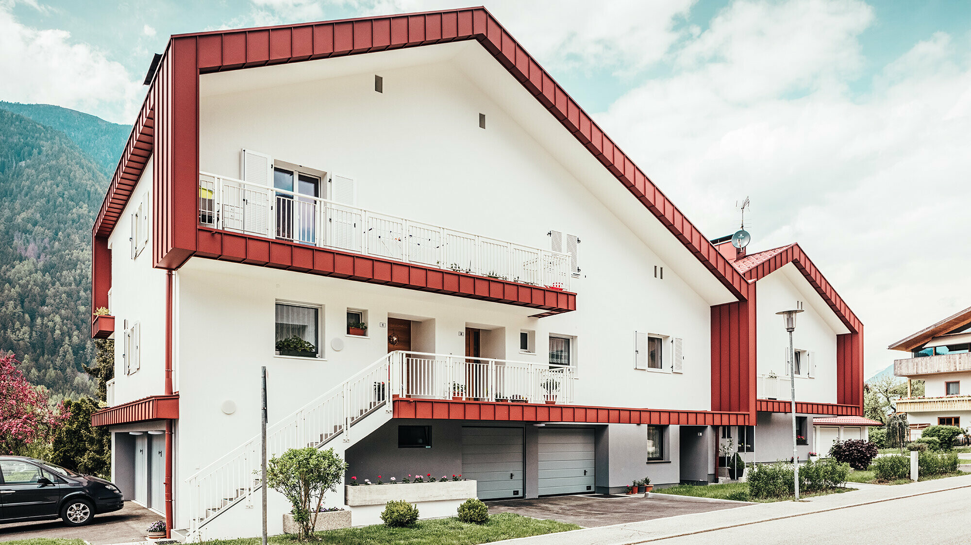 Nachher-Foto des Wohnbaus in Gais: Die oxydrote Dachplatte umrahmt die zwei aneinandergrenzenden Wohnhäuser.