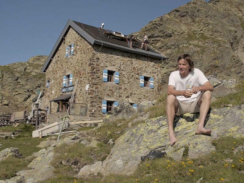 Der Hüttenwirt der Flagger Schartenhütte in Südtirol, Martin Niederkofler, sitzt auf einem Stein vor seiner Hütte und erzählt, als ein Sturmschaden sein Dach beschädigt hat. Jetzt lässt er das sturmsichere PREFA Dach verlegen.