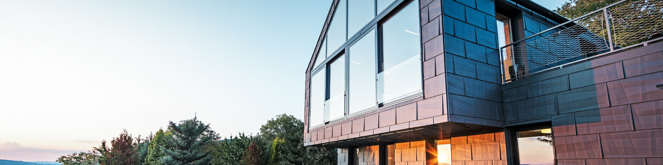 Aluminiumfassade eines Einfamilienhauses mit PREFA Fassadenpaneelen FX.12 in P.10 Anthrazit bei Sonnenuntergang. 