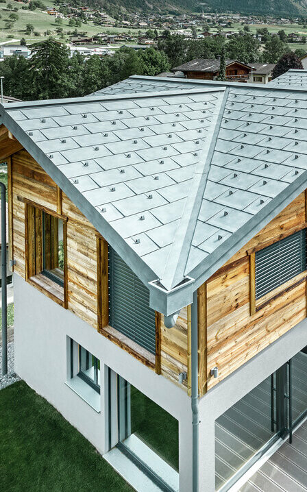 Schweizer Chalet mit einem Aludach von PREFA. Verlegt wurde die Dachplatte R.16 in Steingrau. In der oberen Etage wurde eine rustikale Holzfassade angebracht.