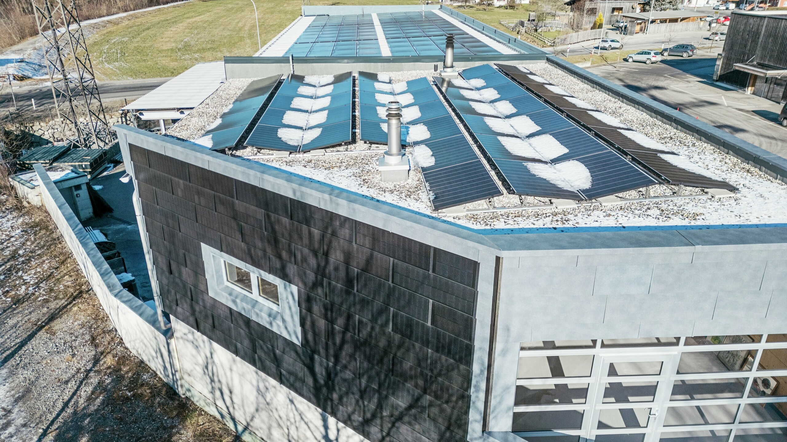 Auf dem Bild kann man das Firmengebäude der Firma RÜMA in Vorarlberg aus der Vogelperspektive sehen. An der Fassade wurde die PREFA Solardachplatte für eine nachhaltige Stromerzeugung angebracht.