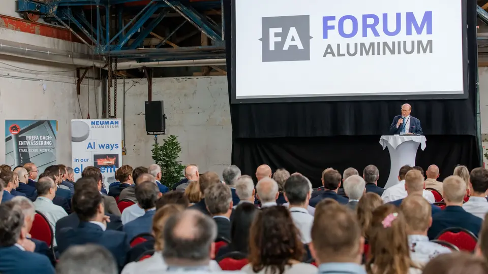 Große Bühne beim Forum Aluminium mit beeindruckender Leinwand und „FA Forum Aluminium“-Logo als zentralem Eyecatcher. Vor industrieller Kulisse des Glanzstoff-Geländes in St. Pölten spricht Dr. Cornelius Alexander Grupp am Rednerpult zu einem dicht besetzten Publikum aus Branchenexperten und Entscheidern. Banner zu Aluminiumlösungen und innovative Anwendungen unterstreichen die thematische Tiefe. Die Szene zeigt den intensiven Austausch zu Zukunftstechnologien, Recycling und Marktentwicklungen und vermittelt die dynamische Atmosphäre einer hochkarätigen Fachkonferenz.