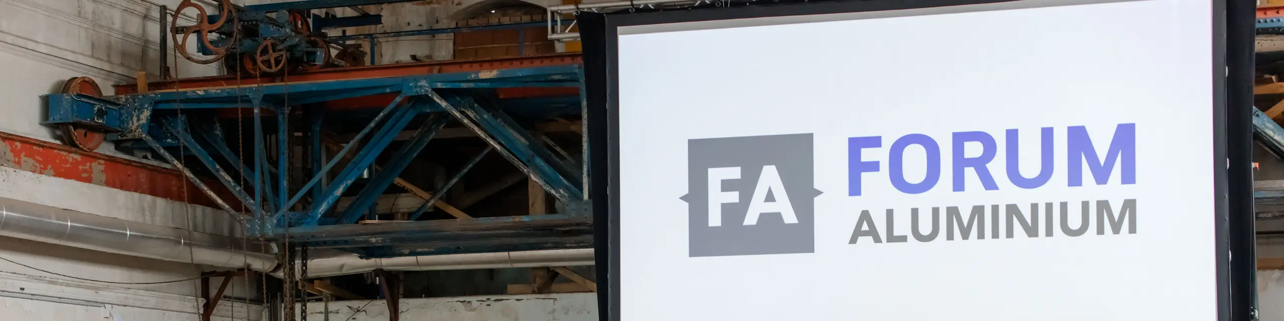 Große Bühne beim Forum Aluminium mit beeindruckender Leinwand und „FA Forum Aluminium“-Logo als zentralem Eyecatcher. Vor industrieller Kulisse des Glanzstoff-Geländes in St. Pölten spricht Dr. Cornelius Alexander Grupp am Rednerpult zu einem dicht besetzten Publikum aus Branchenexperten und Entscheidern. Banner zu Aluminiumlösungen und innovative Anwendungen unterstreichen die thematische Tiefe. Die Szene zeigt den intensiven Austausch zu Zukunftstechnologien, Recycling und Marktentwicklungen und vermittelt die dynamische Atmosphäre einer hochkarätigen Fachkonferenz.