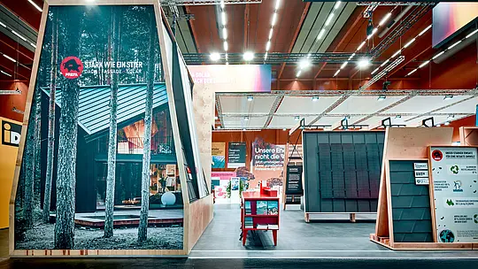 PREFA Messestand 2026 mit kraftvoller Markeninszenierung: Das Motto „Stark wie ein Stier“ prägt den ersten Eindruck und unterstreicht die robuste Qualität der PREFA Produkte für Dach, Fassade und Solar. Eine großformatige Fassadenabbildung mit moderner Architektur und Aluminiumdach zeigt anschaulich die gestalterische Vielfalt des Systems. Rechts im Bild: Solarlösungen, Dachsysteme und ein Infoboard zu Nachhaltigkeit und Umweltschutz. Der Stand überzeugt durch klare Struktur, hochwertige Präsentation und starke visuelle Botschaften – ein Blickfang für Bauherren, Planer und Verarbeiter, die langlebige, klimafitte Lösungen suchen. PREFA setzt neue Maßstäbe in Design, Funktion und Energieeffizienz.