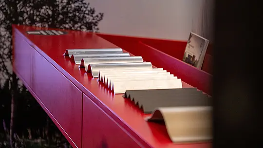 Auf der Architect@Work Messe in der Wiener Stadthalle werden hochwertige Strangpressprofile aus Aluminium präsentiert. Die Nahaufnahme zeigt die verschiedenen Formen – von Welle bis Zacke – und Oberflächen der PREFA Aluminiumprodukte auf einer markanten, roten Präsentationsfläche. Die vielseitigen Bauelemente verdeutlichen präzises Design, langlebige Qualität und innovative Lösungen für moderne Architektur unter Verwendung nachhaltiger Materialien.