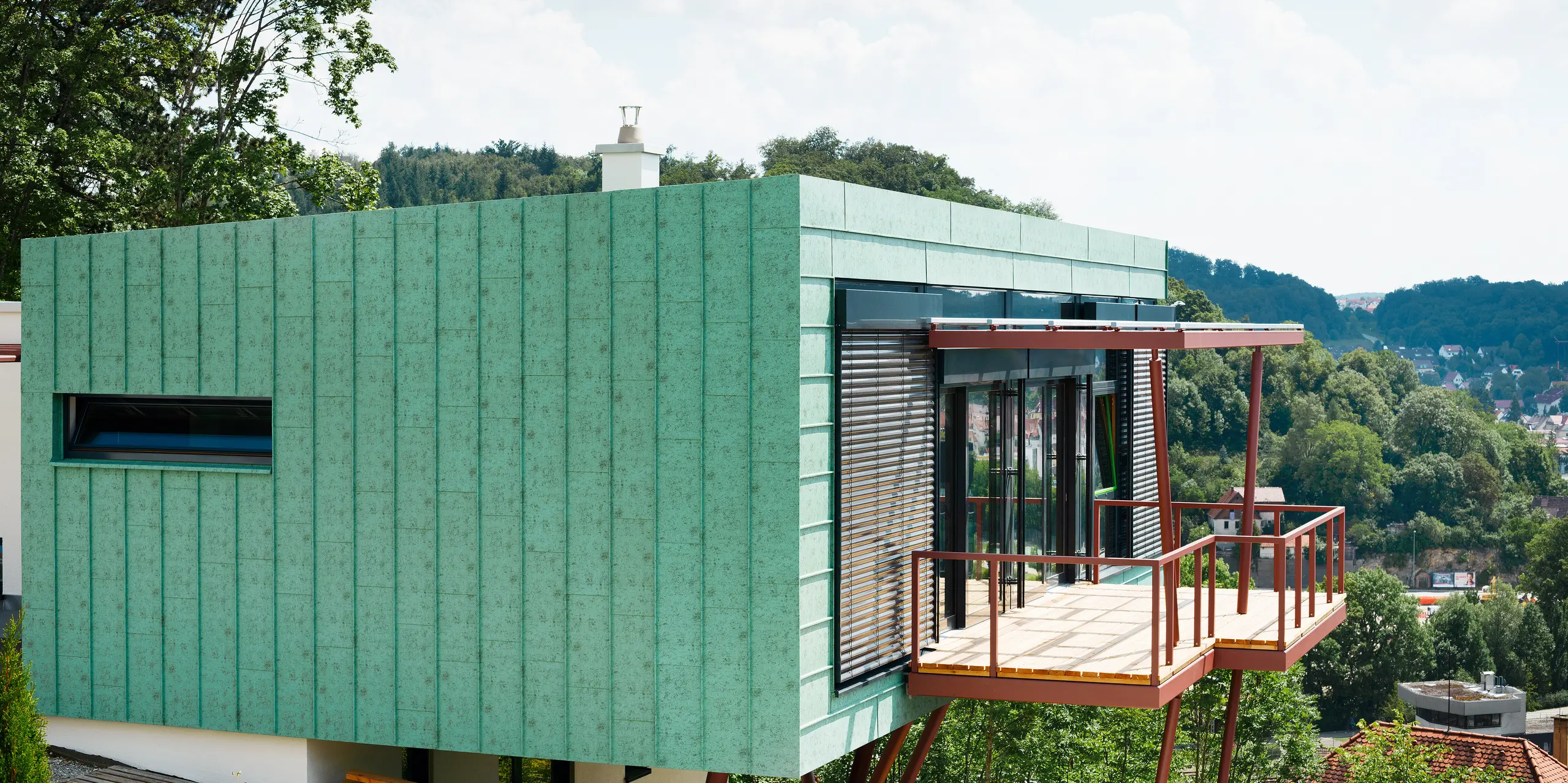 Das Heidenheimer Wohnhauses wird umhüllt von einer markanten PREFALZ-Fassade in Patina-Grün, die in der Sonne glänzt. Die perfekte Kombination aus Funktionalität und Design wird durch die widerstandsfähigen Eigenschaften der PREFALZ-Fassade verstärkt. Sie trotzt nicht nur dem Wetter, sondern garantiert auch eine lange Lebensdauer. Diese Fassade hebt die Schönheit und Beständigkeit des Gebäudes auf ein neues Niveau.