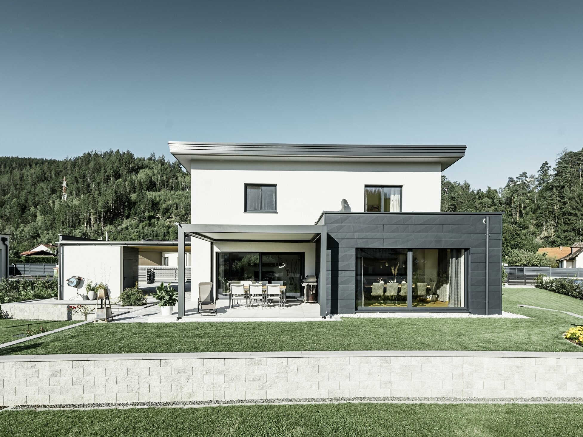 Neu gebautes Einfamilienhaus mit Zubau; Anbau hebt sich optisch vom Rest des Hauses ab, da er mit dem PREFA Fassadenpaneelen Siding.X in Anthrazit verkleidet ist. Der Rest der Fassade ist weiß verputzt.