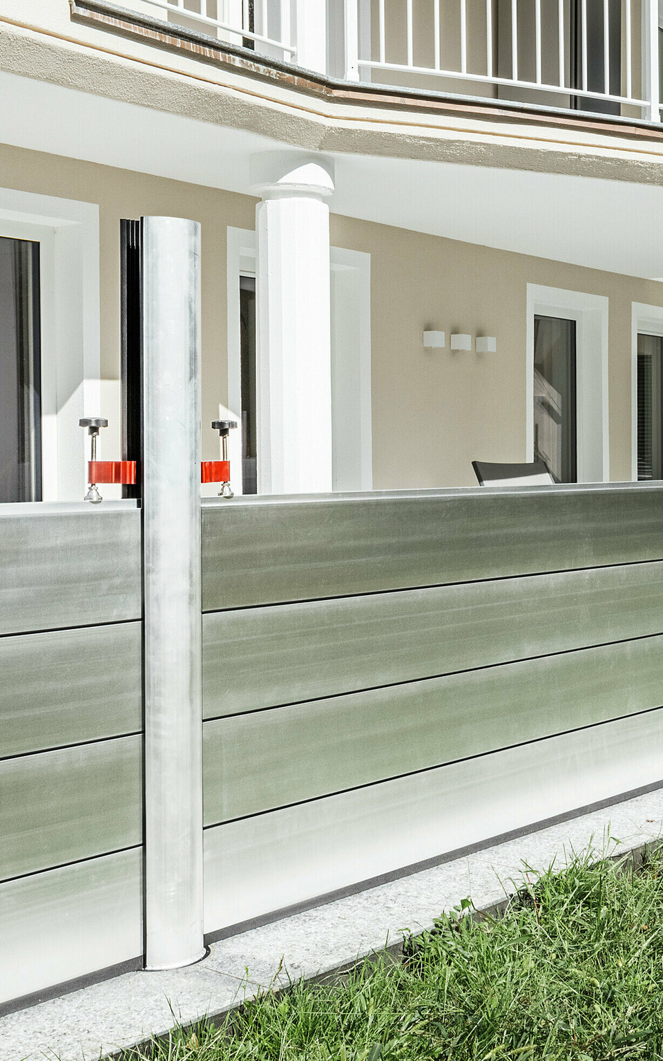 Panoramaansicht eines exklusiven Wohnhauses in Tirol mit installiertem PREFA Hochwasserschutzsystem entlang der Terrasse. Die Dammbalken aus Aluminium verlaufen über die gesamte Gebäudelänge und schützen mehrere Zugänge wie Terrassentüren und Fenster vor möglichem Hochwasser aus dem angrenzenden Gelände. Die moderne Architektur des Hauses mit Rundbalkon und weißen Stützen bildet einen stilvollen Kontrast zum funktionalen Hochwasserschutz aus Aluminium.