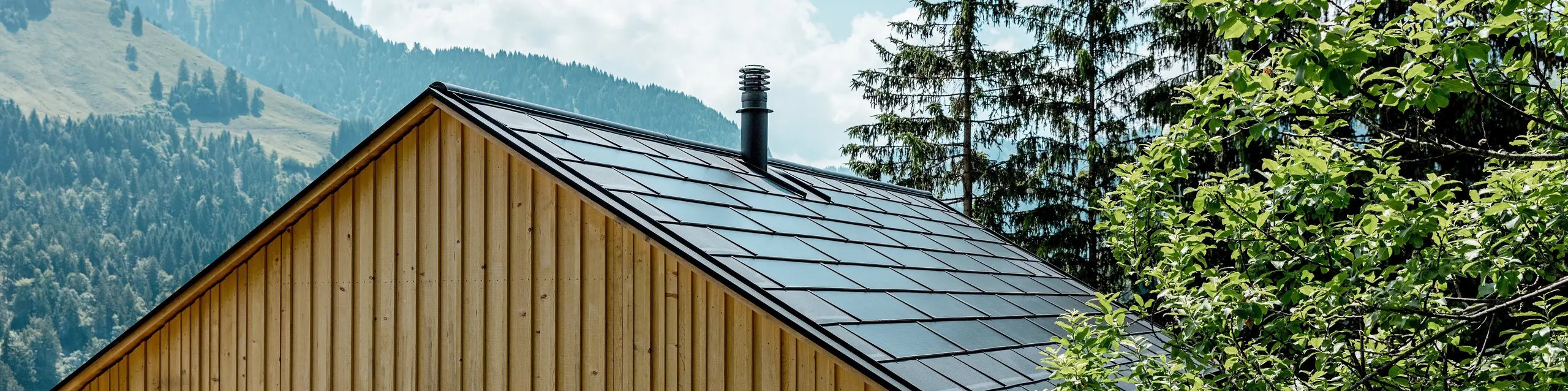 Zwischen grünen Baumkronen und eindrucksvoller Bergkulisse zeigt sich Haus Immi als moderner Rückzugsort im alpinen Ebnit. Die naturbelassene Weißtannenfassade trifft auf ein elegantes PREFA Solardach in P.10 Schwarz. Integrierte Solardachplatten und Dachplatten R.16 verbinden nachhaltige Stromerzeugung, robusten Wetterschutz und eine klare, harmonisch in die Landschaft eingebettete Architektur für höchste Ansprüche.