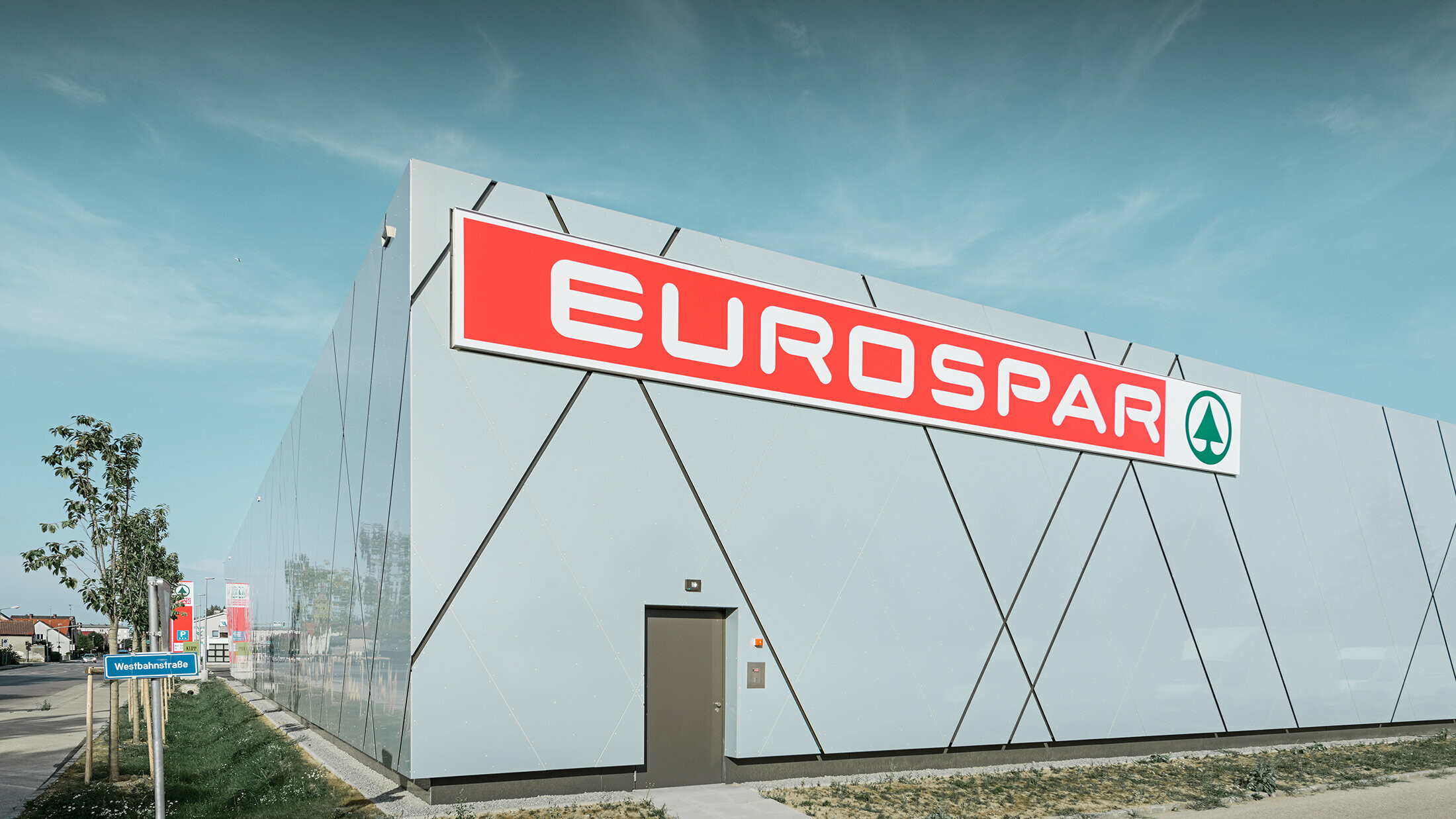 Die Rückseite des Gebäudes präsentiert das großflächige Eurospar-Logo auf einer glatten PREFA Aluminiumfassade. Die Sonderfarbe Silver Gold und die diagonalen Fugen setzen ein modernes Statement und machen die Filiale zum optischen Blickfang im Stadtbild von Wels.