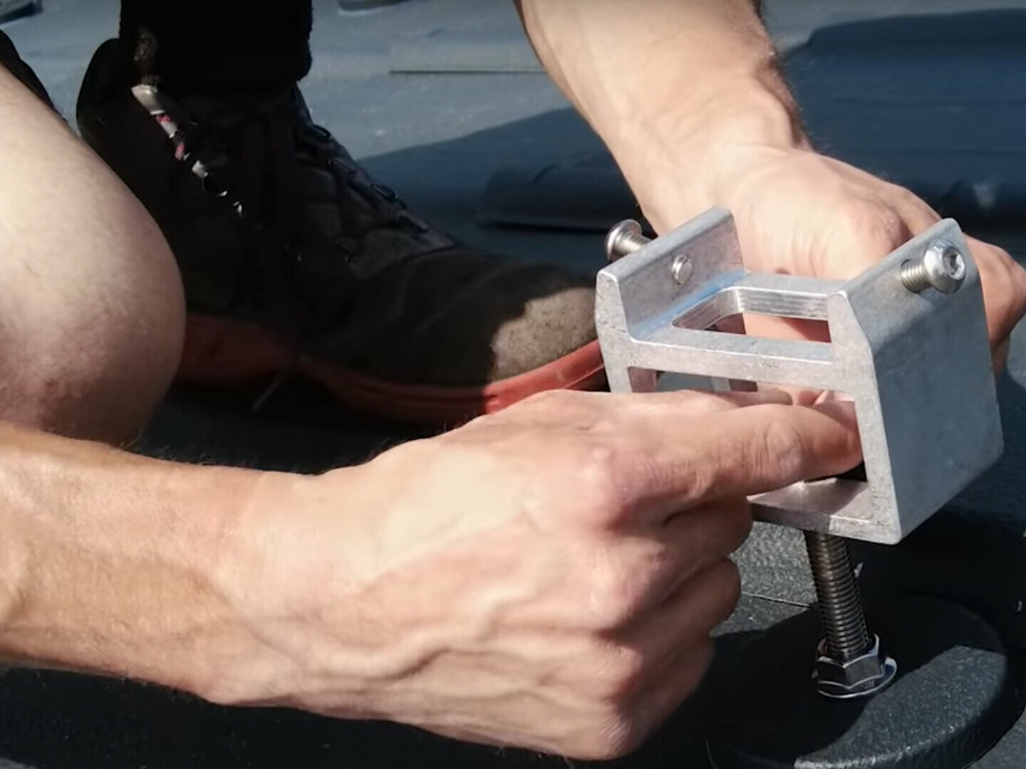 Eine Person montiert einen PREFA Solarhalter auf einem Flachdach. Sie sitzt und benutzt beide Hände, um eine leichte Aluminiumhalterung sorgfältig zu justieren, die dazu dient, Solarpaneele sicher zu befestigen. 