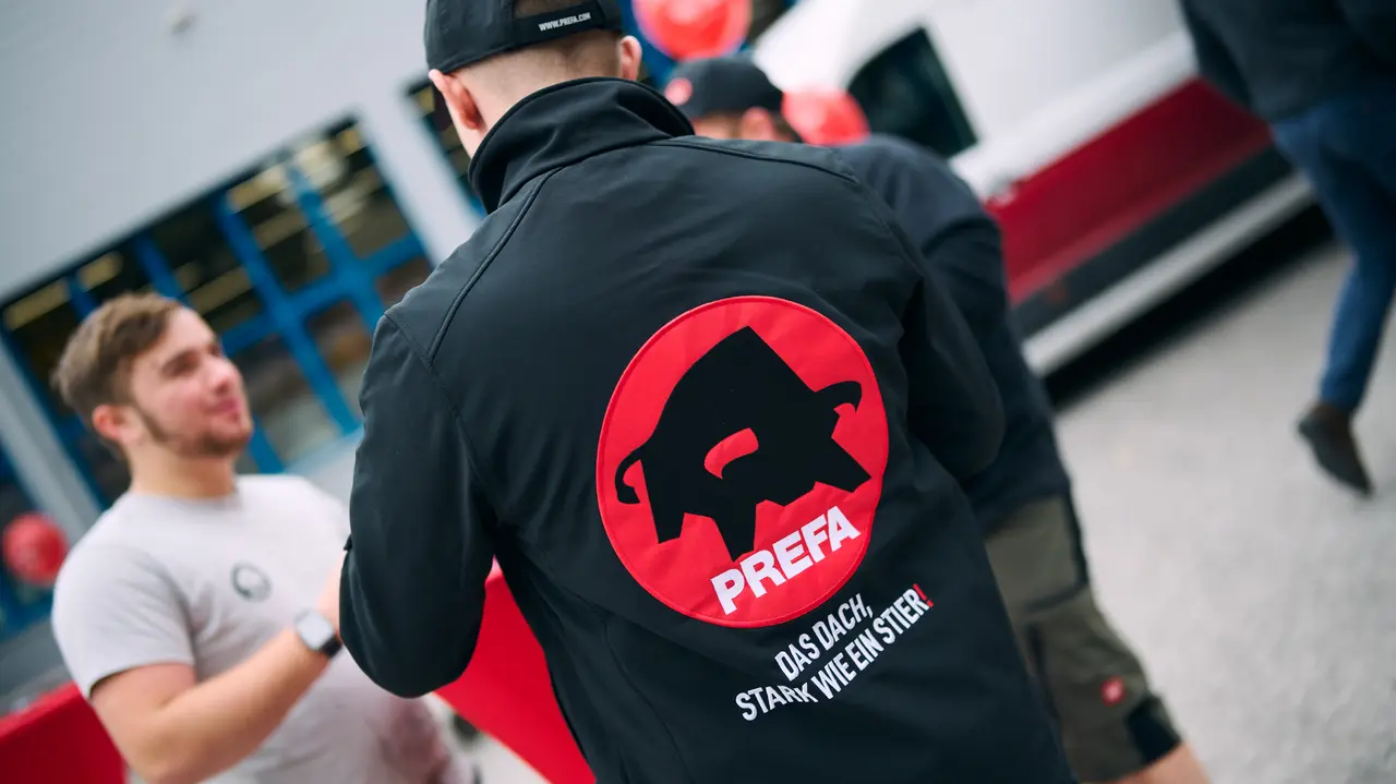 PREFA Mitarbeiter bei einem Karriere-Event mit gebrandeter Arbeitskleidung und Logo, im Austausch mit potenziellen Bewerbern vor dem Unternehmensgebäude.