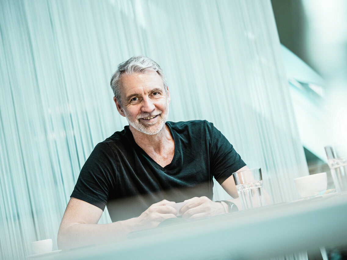 Porträt des Architekten Oliver Kupfner, lächelnd und entspannt, sitzend an einem Tisch