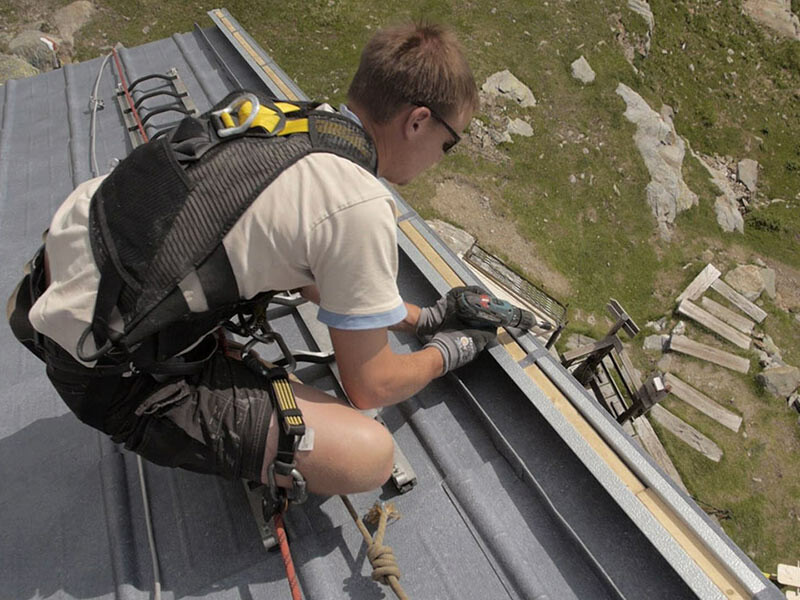 Spengler arbeitet am Ortgang an der neuen Dacheindeckung der Flagger Schartenhütte in Südtirol. Verlegt wird die PREFA Dachplatte in steingrau.