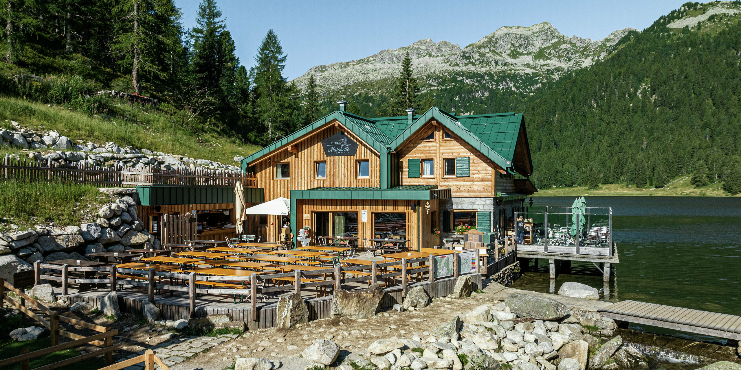 Das Rifugio Malghette auf 1.888 m, direkt am See gelegen, mit wetterfestem PREFALZ Dach in P.10 Moosgrün. Die langlebige Aluminiumeindeckung schützt die Hütte vor extremen Witterungseinflüssen und fügt sich perfekt in die alpine Landschaft ein. Die großzügige Sonnenterrasse bietet einen einzigartigen Ausblick auf die umliegende Bergwelt.