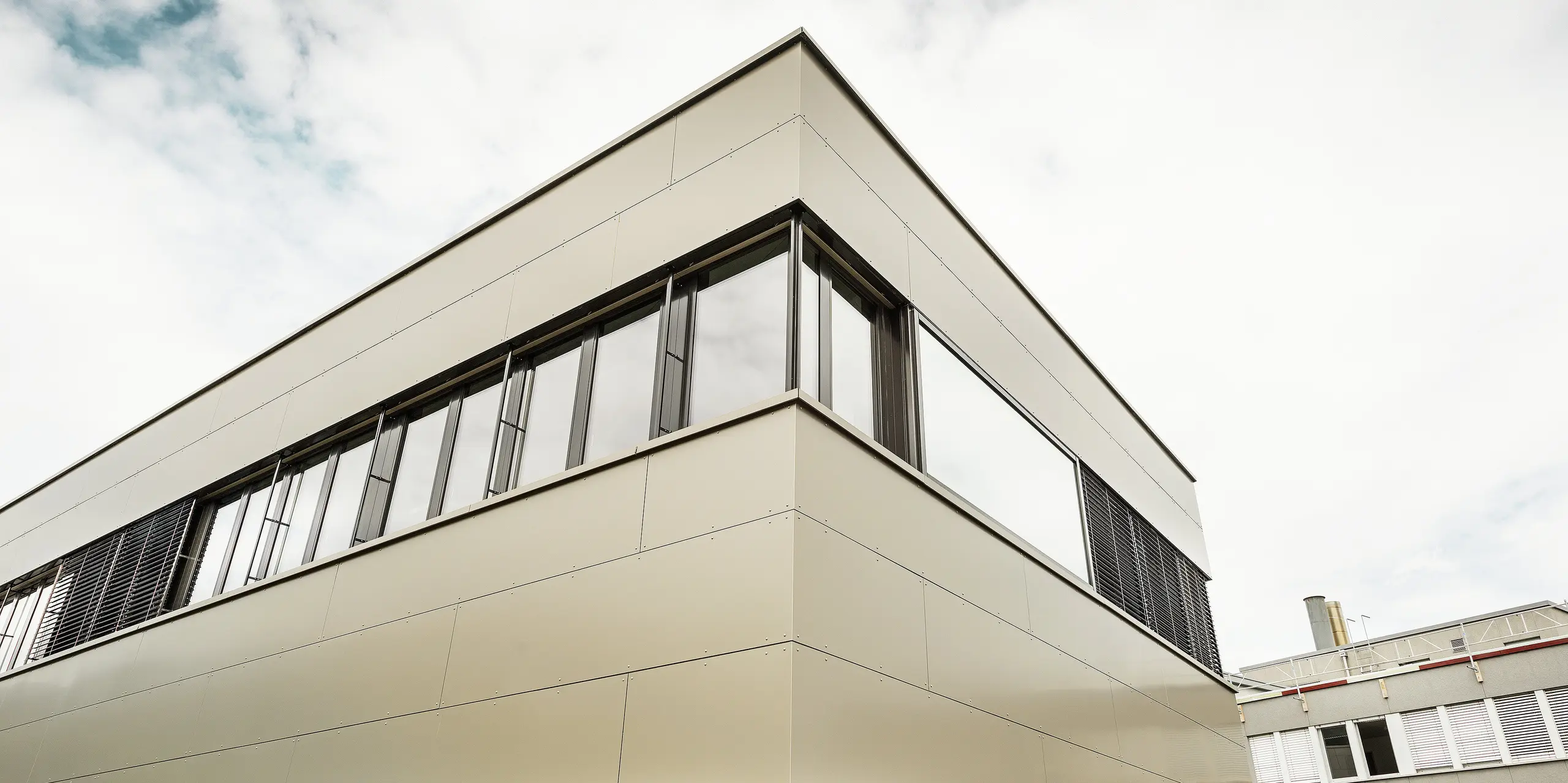 Die Nahaufnahme der Gebäudeecke zeigt die hochwertige PREFA Aluminiumfassade mit klar definierten Fugenbildern. Die edle Bronzefarbe der Aluminium Verbundplatten verleiht dem Firmengebäude eine exklusive, langlebige Außenwirkung.