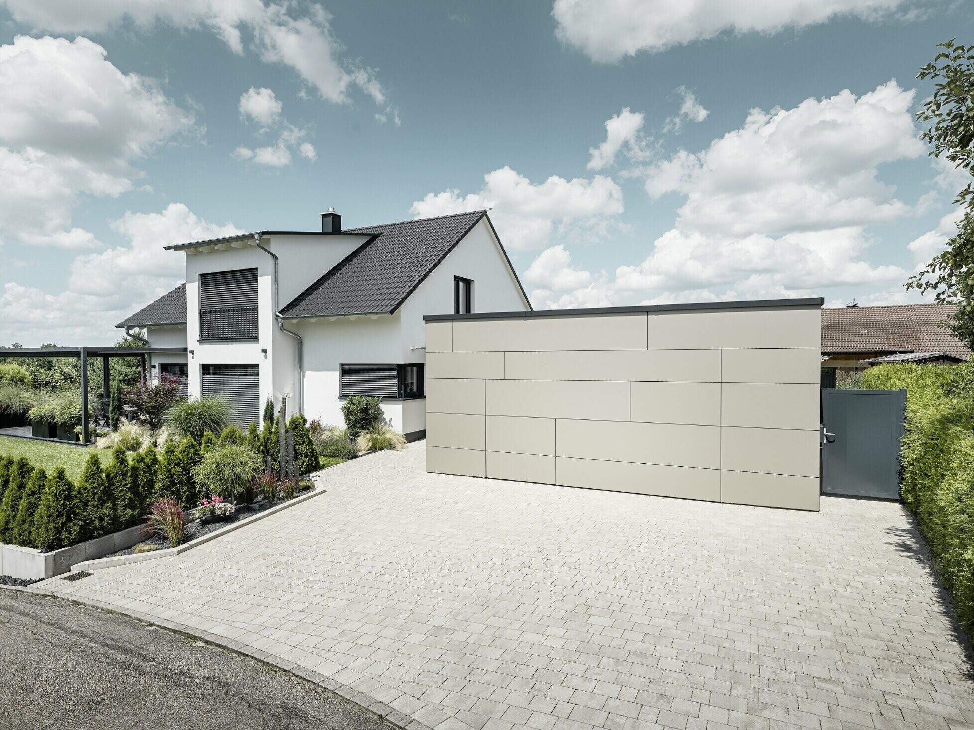 Die Garage des Einfamilienhauses ist an der Fassade komplett mit der Aluminium Verbundplatte in Bronze verkleidet. Auch das Garagentor ist mit den Fugen nicht erkennbar. Davor ist eine großzügige Einfahrt.