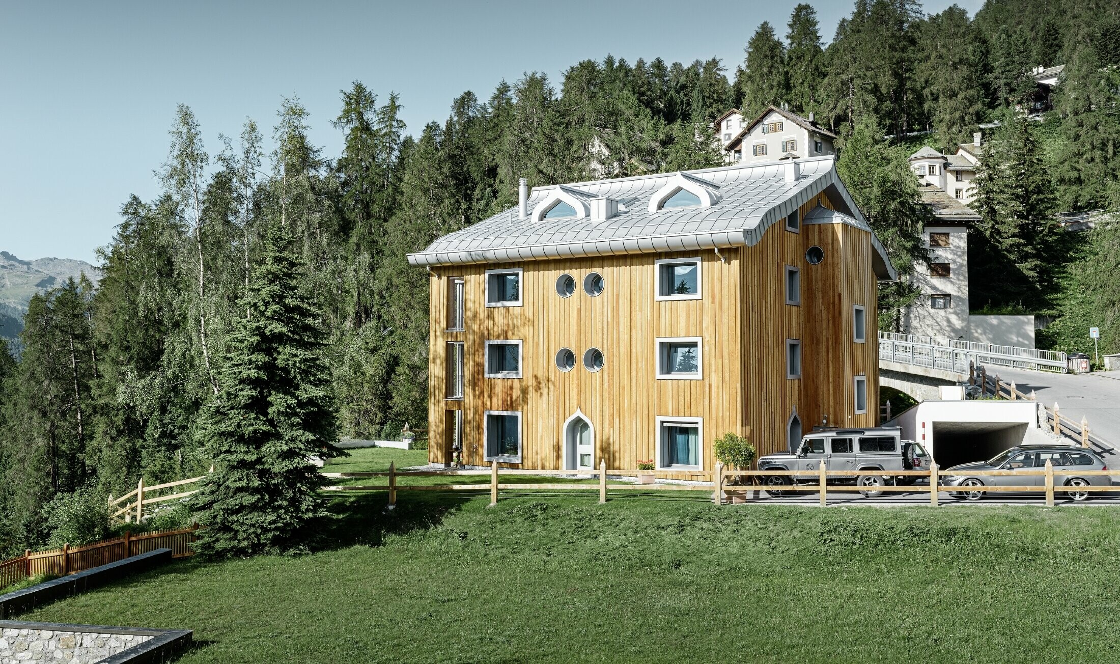 Wohnhausanlage in St. Moritz mit Holzfassade und Aluminiumdach mit geschwungener Traufe in silbermetallic