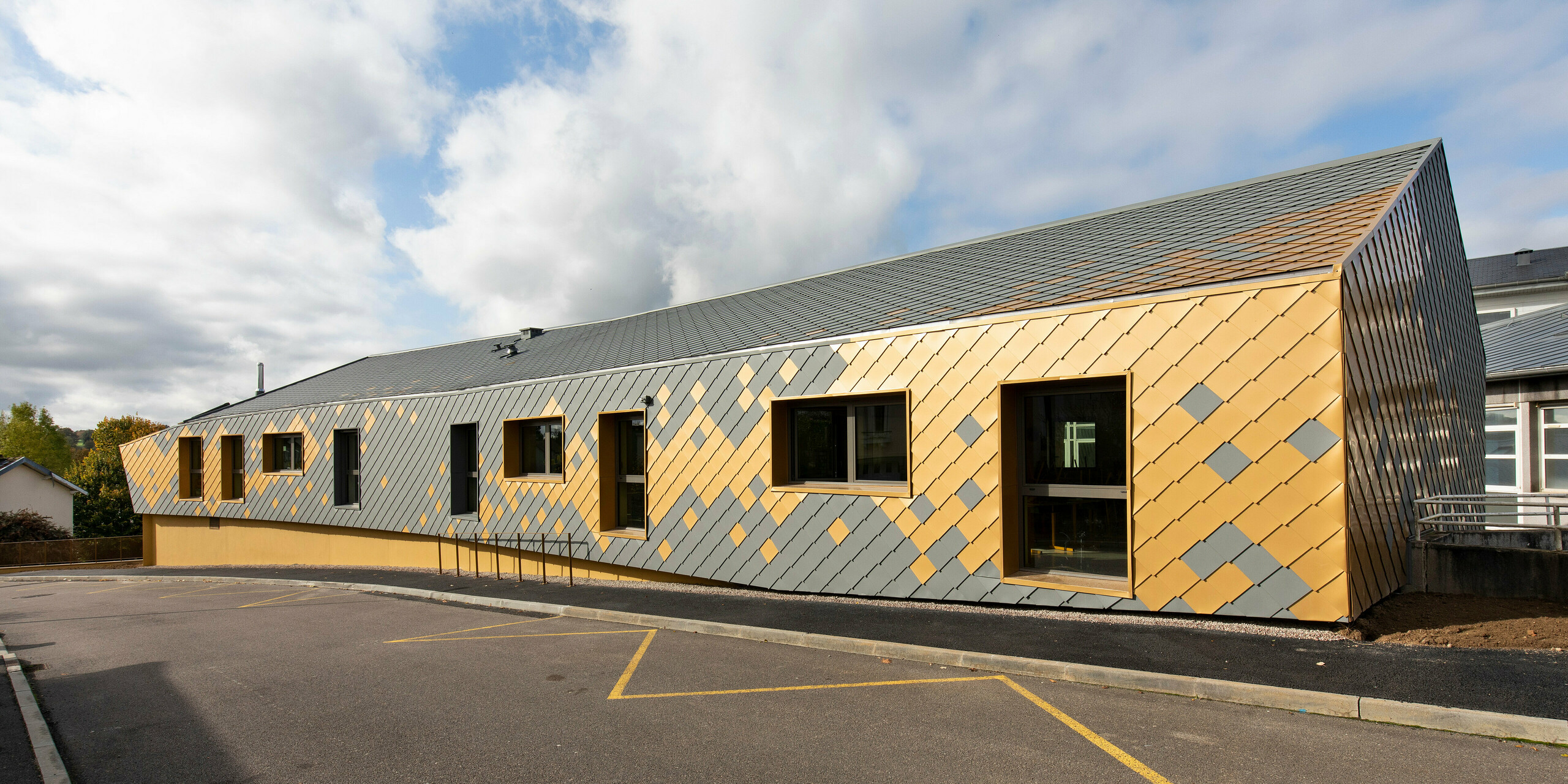 Seitenansicht der Grundschule in Pierre-Buffière mit einer Fassade aus PREFA Wandrauten 29 × 29 in P.10 Hellgrau und der Sonderfarbe Mayagold
