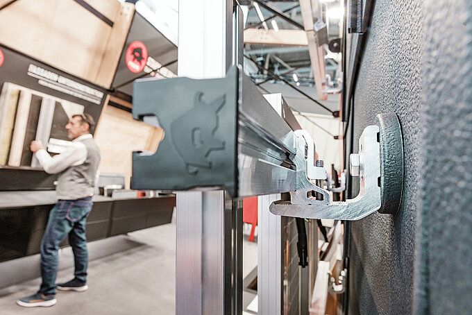 Das Solar-Montagesystem PREVARIO von PREFA im Detail: Die robuste Aluminiumstütze ermöglicht eine stabile Montage auf unterschiedlichen Dachkonstruktionen. Langlebig, korrosionsbeständig und ideal für eine effiziente und zeitsparende Photovoltaik-Montage. Der Blick von der Seite eröffnet eine spannende Perspektive auf das stabile PV-Montagesystem. Im Hintergrund ist ein PREFA Mitarbeiter zu sehen. Die Aufnahme entstand im Rahmen der BAU München 2025, wo das innovative Produkt erstmals präsentiert wurde.