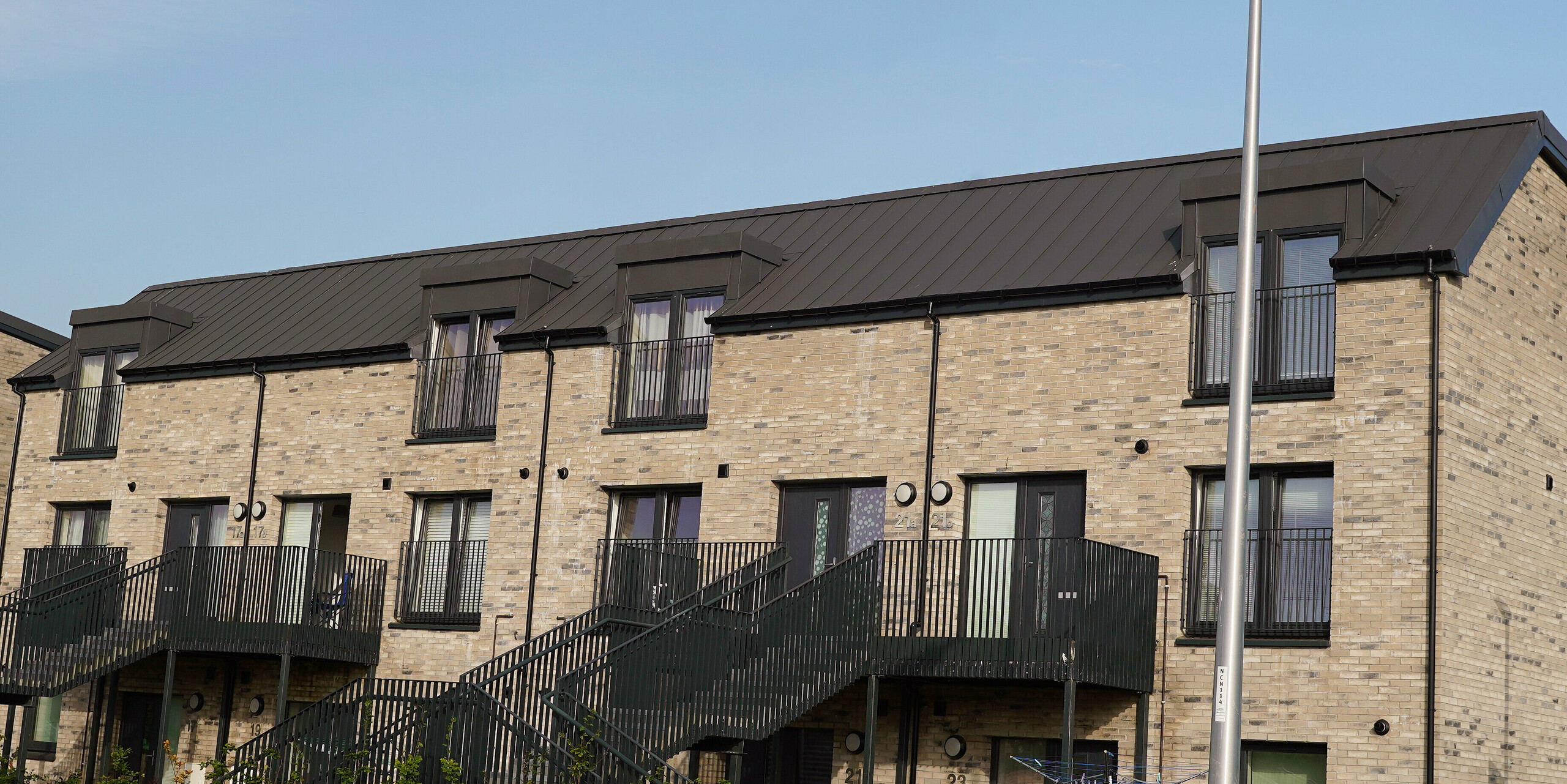 Detailansicht einer modernen Wohnhausanlage in Edinburgh, Schottland, mit einer hochwertigen PREFALZ Dacheindeckung in P.10 Dunkelgrau. Die langlebigen Aluminiumdächer von PREFA bieten eine optimale Kombination aus Funktionalität und ästhetischem Design, das sich nahtlos in die städtische Architektur integriert. Die sichtbare Materialqualität und präzise Verarbeitung der PREFALZ Produkte tragen zur Wertsteigerung der Immobilie bei und unterstreichen die Nachhaltigkeit moderner Bauprojekte. Als Gegenstück zum zeitgemäßen Dach ziert das Bauwerk eine traditionelle Backsteinfassade.