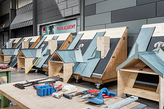 Innenräume des PREFA Schulungszentrums in Rheinbach (DE). Hier stehen viele Dachmodelle, an denen die Schulungsteilnehmer die richtige Verlegung und Montage von PREFA Produkten üben können. Ein geschulter Lehrverleger steht ihnen dabei zur Seite. 