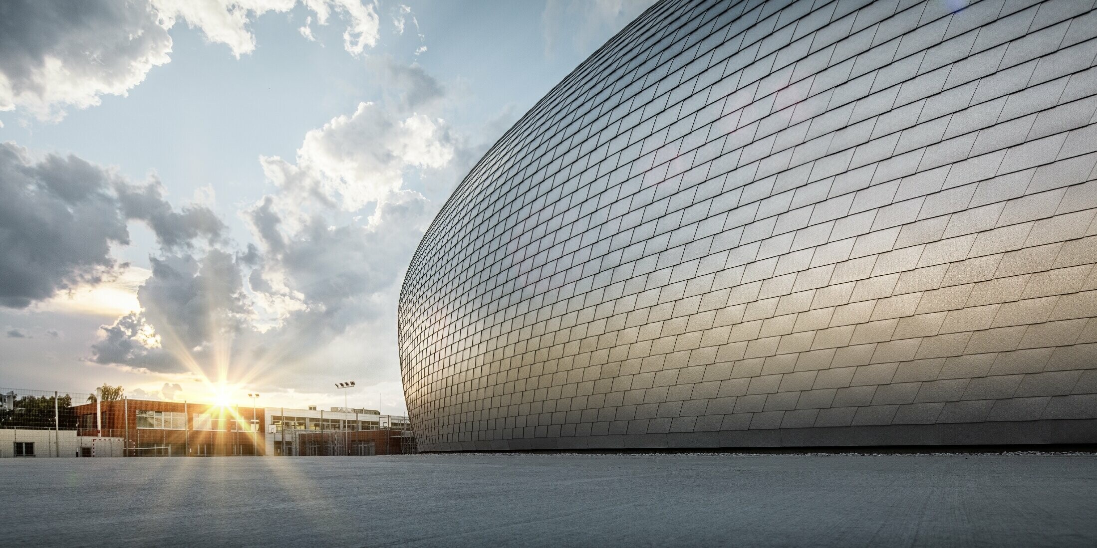 Sporthalle in Tschechien in Form eines UFOs verkleidet mit der PREFA Wandschindel in Naturblank bei Sonnenaufgang.