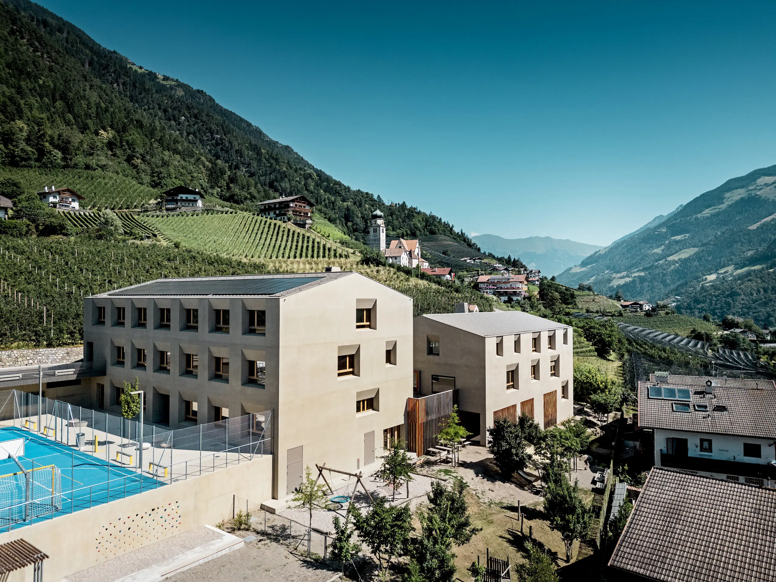 Das Bildungszentrum Riffian in Südtirol zeigt Kindergarten und Volksschule als harmonisches Architekturensemble inmitten der Berglandschaft. Die PREFA Dachrauten 44 × 44 in P.10 Bronze verleihen den Gebäuden eine elegante Optik, bieten langlebigen Witterungsschutz und fügen sich präzise in die natürliche Umgebung ein.