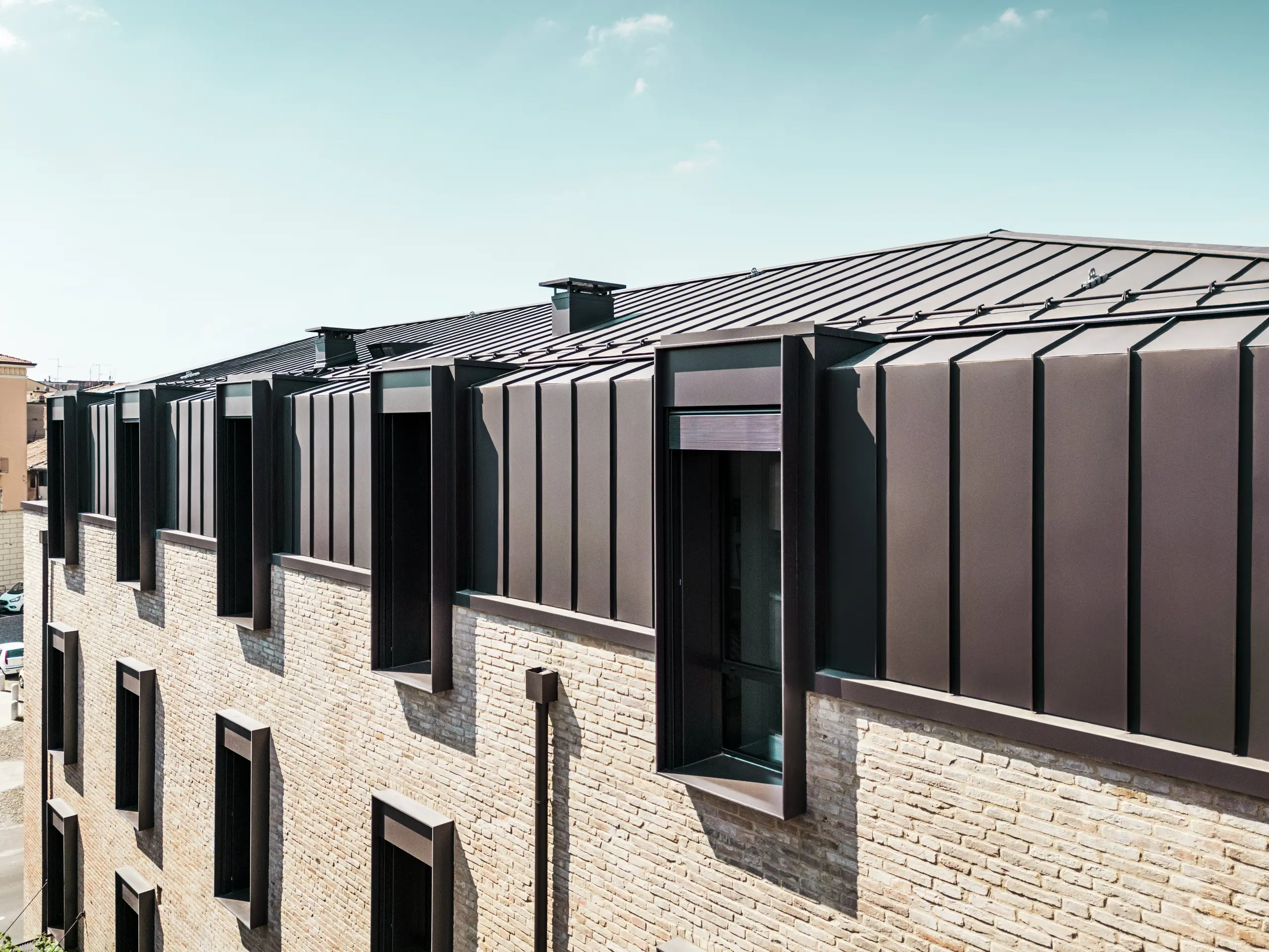 Modernes Dach- und Fassadendesign eines Backsteinhauses in Italien mit PREFALZ Aluminiumdach in P.10 Haselnussbraun und markanten Oberlichtern (Giebeln).
