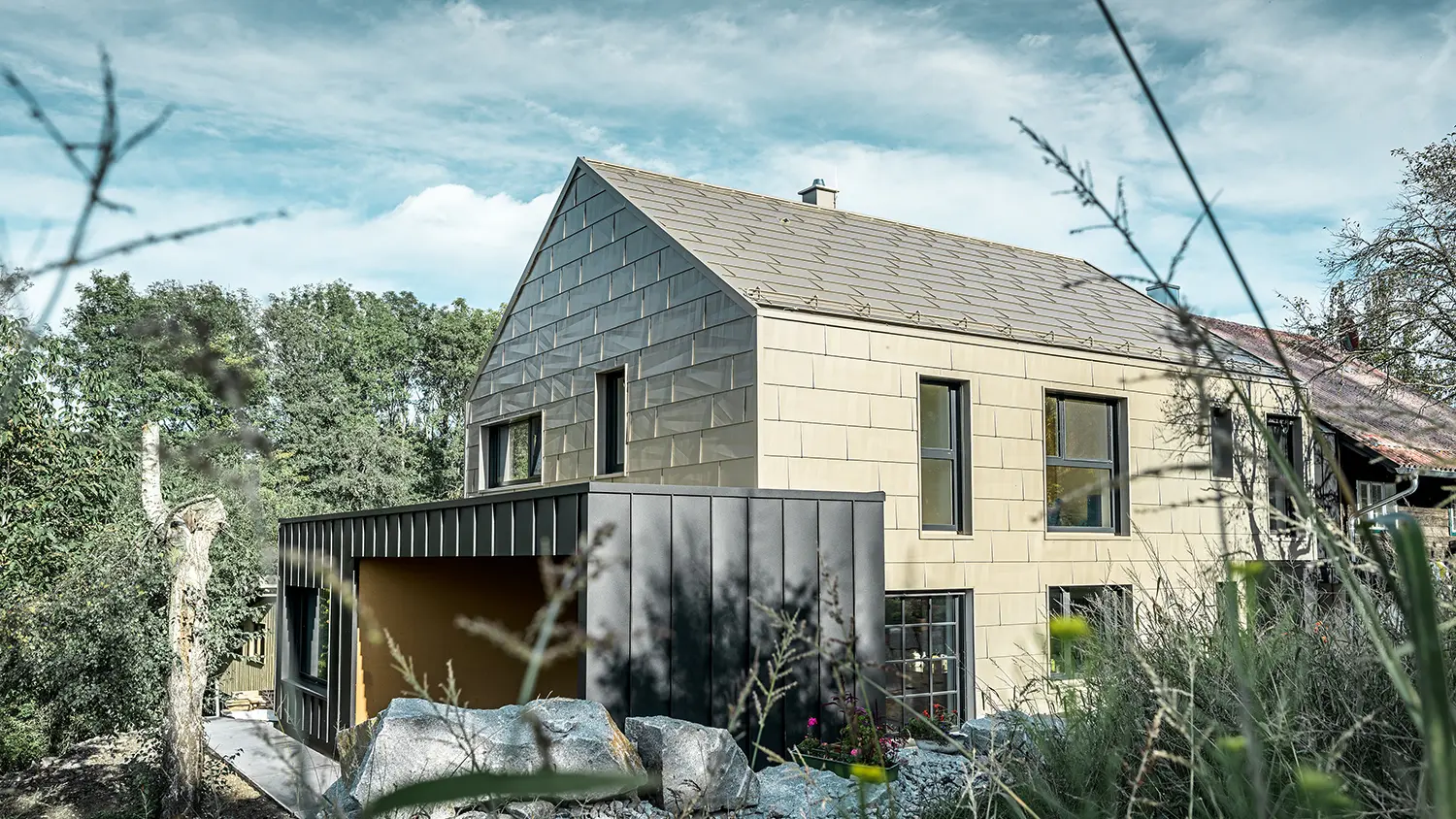 Wohnhaus ohne Dachvorsprung ist am Dach und der Fassade mit dem Aluminium Paneel FX.12 von PREFA in Bronze verkleidet. Gleich daneben steht eine Garage mit Flachdach mit einer Winkelstehfalzfassade.