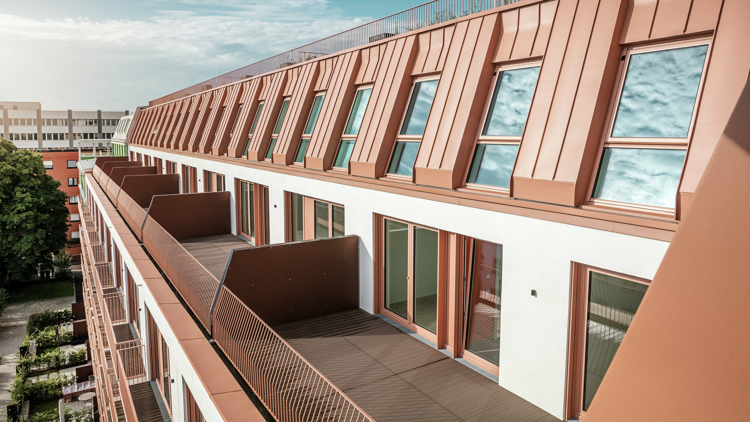 Detailansicht der modernen Dach- und Fassadengestaltung des Wohnprojektes Van B in München mit dem hochwertigen PREFALZ Aluminiumdach in IGP Orange HDP von PREFA. Die präzise Verarbeitung des langlebigen und wartungsarmen Materials bietet optimalen Schutz vor Witterungseinflüssen und verleiht dem Gebäude ein einheitliches, elegantes Erscheinungsbild. Die großzügigen Fenster und Balkone sorgen für viel Tageslicht und schaffen ein offenes, lebenswertes Wohnambiente mit architektonischem Anspruch.